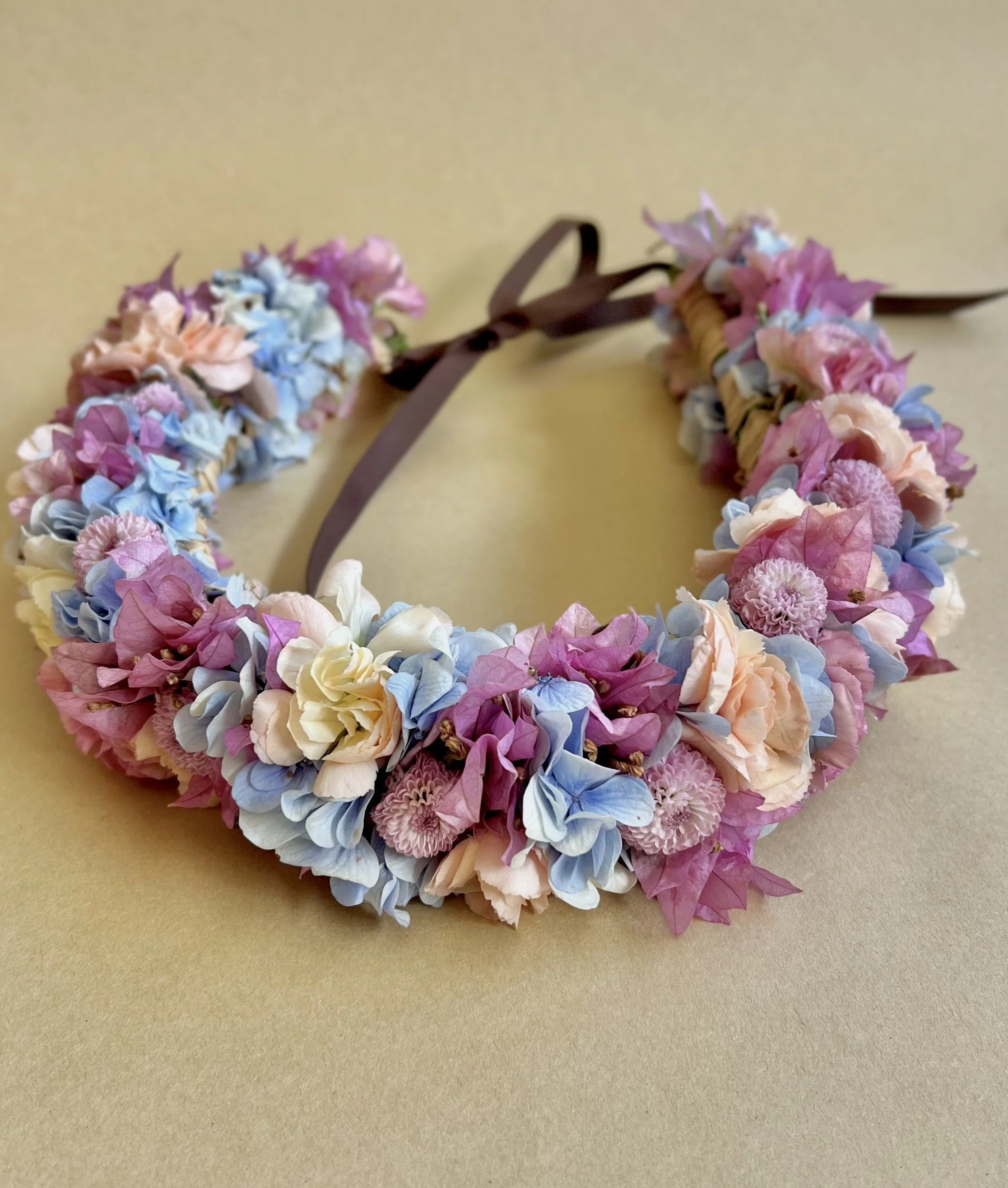 Floral headband made of pink, blue, white, and purple flowers, tied with a brown ribbon.