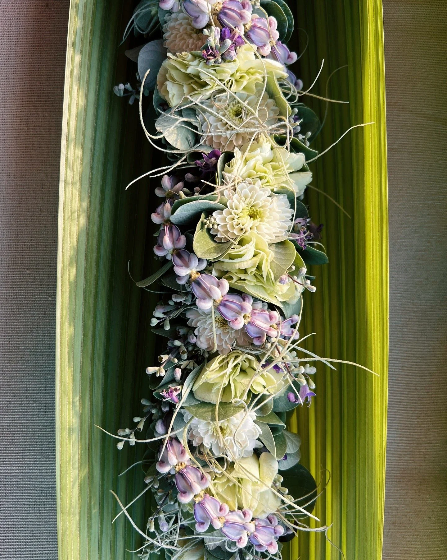 A floral arrangement featuring white, purple, and green flowers on a green rectangular tray with a yellow border.