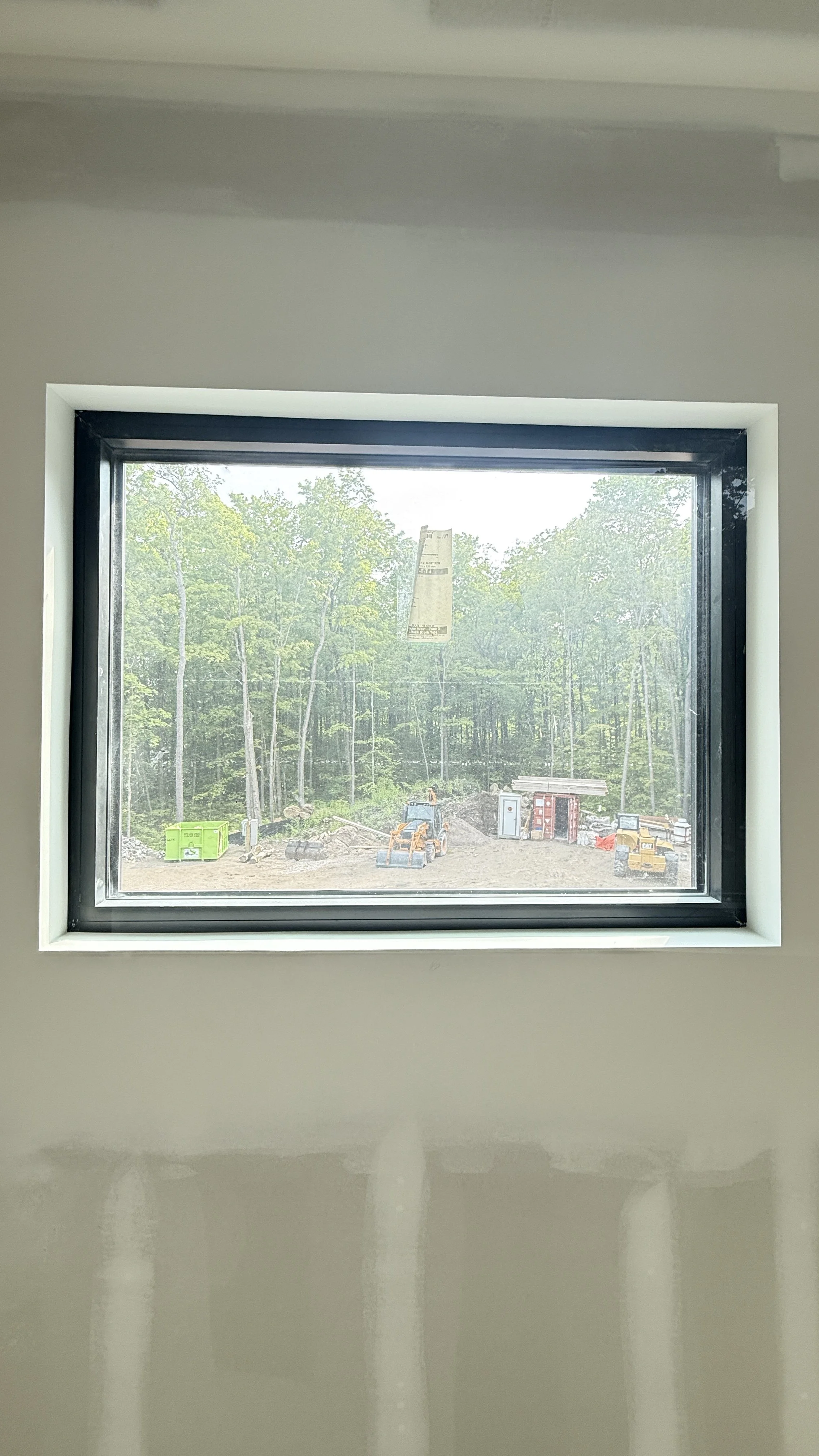 View through a window showing a construction site with trees, construction equipment, and materials.