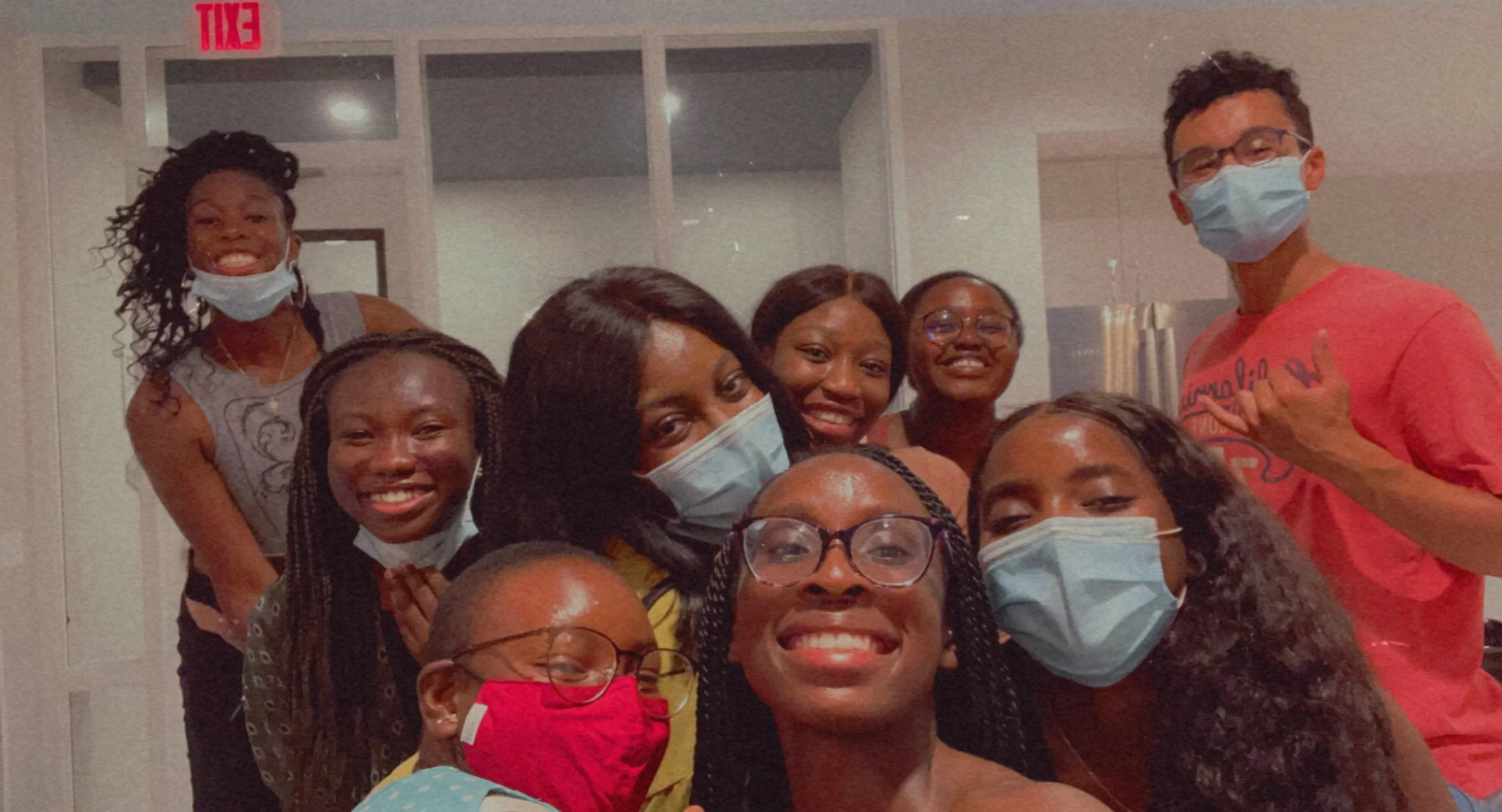 Group of Mope and Robert's friends smiling, some wearing face masks, posing together indoors.