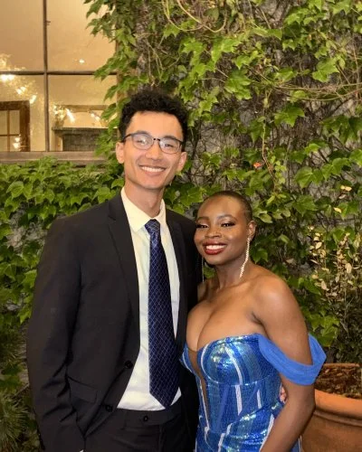 Robert and Mope are dressed formally, smiling and standing outdoors in front of greenery at night.