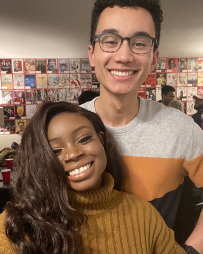 Mope and Robert smiling at a party or gathering, with a wall of magazine covers behind them.