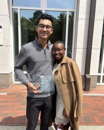 Robert and Mope standing outside a building, smiling, with the young man holding a clear award or plaque.