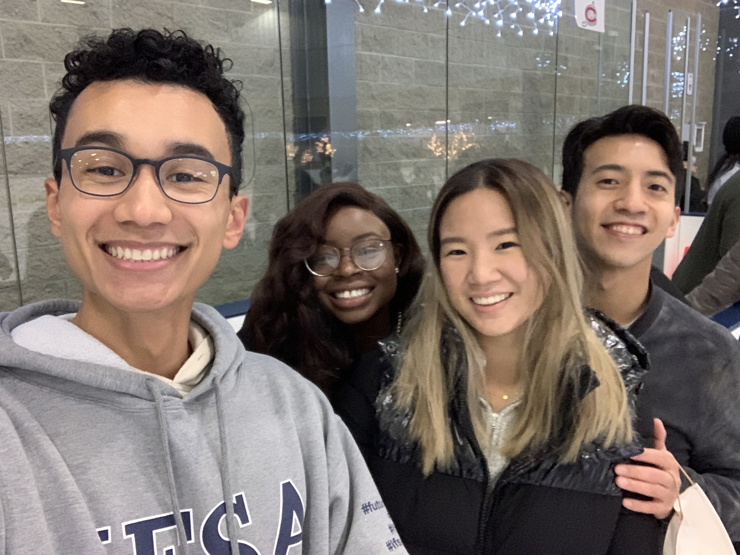 Robert and Mope taking a selfie indoors with friends, with a glass wall and decorative lights in the background.