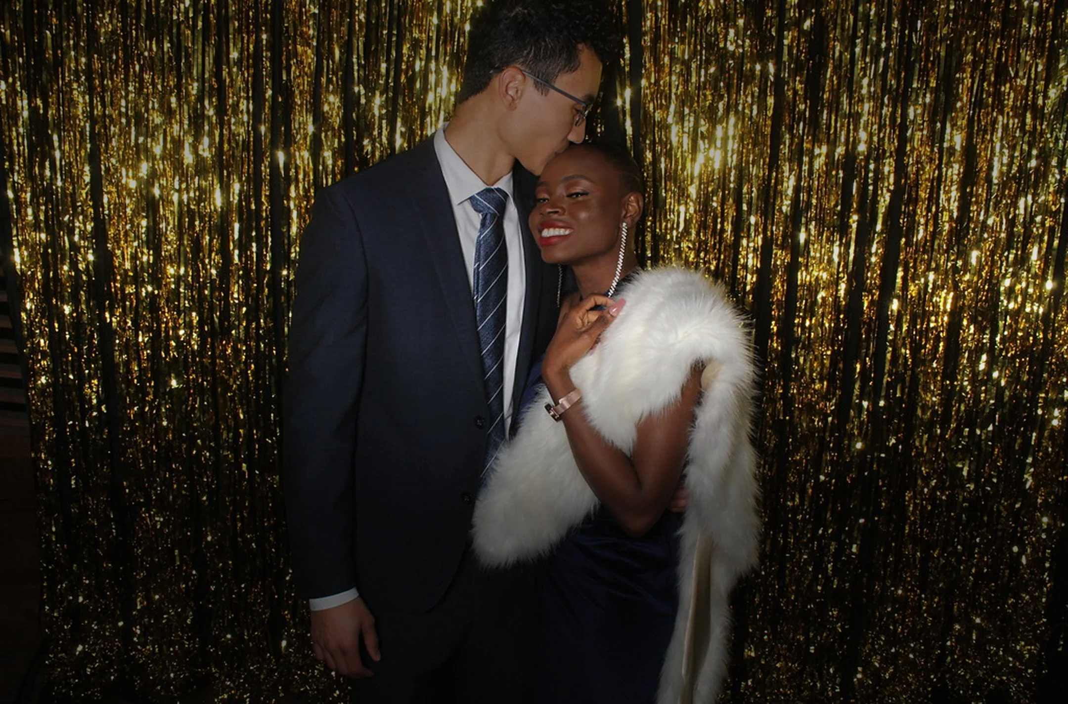 Robert and Mope in formal attire, standing close together in front of a gold glittery backdrop.