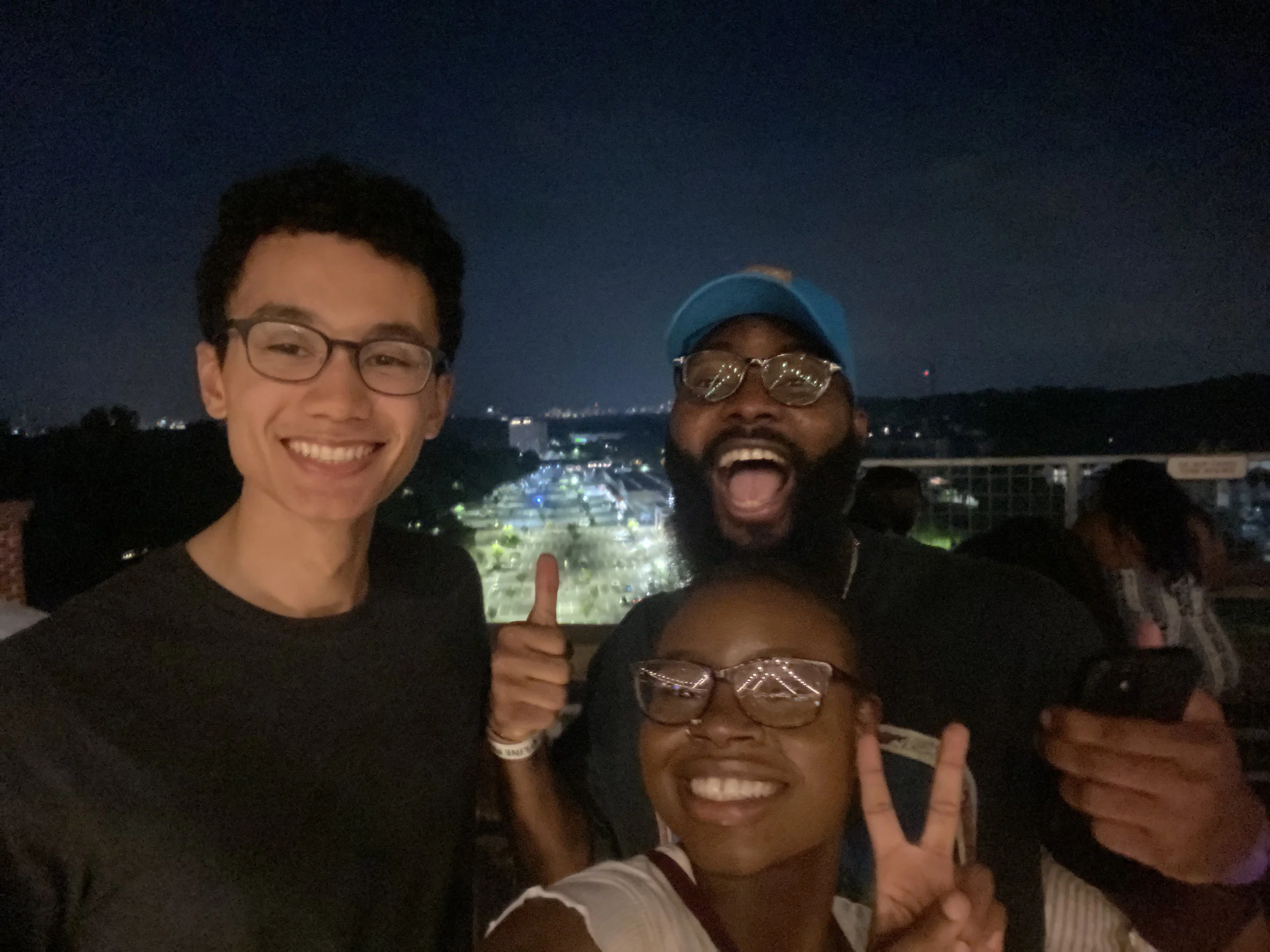 Mope and Robert smiling and posing with their friends at night with a city view in the background.