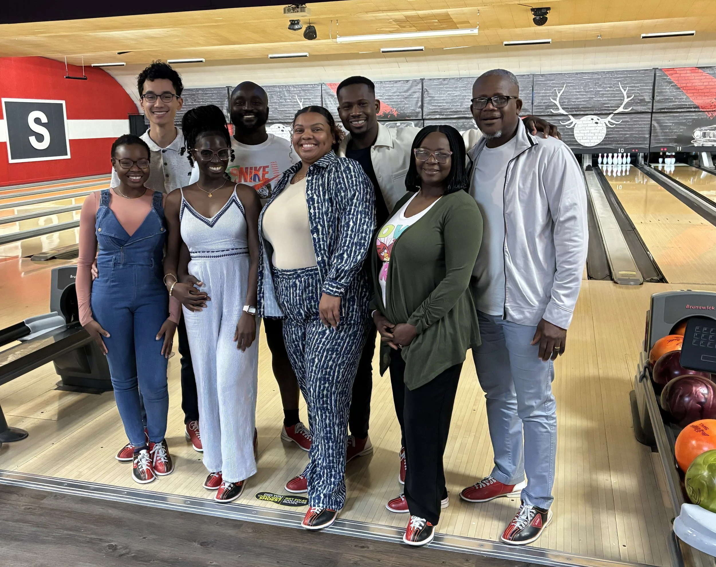 Mope and Robert posing together with Mope's family at a bowling alley, all wearing bowling shoes and standing on the bowling lane.