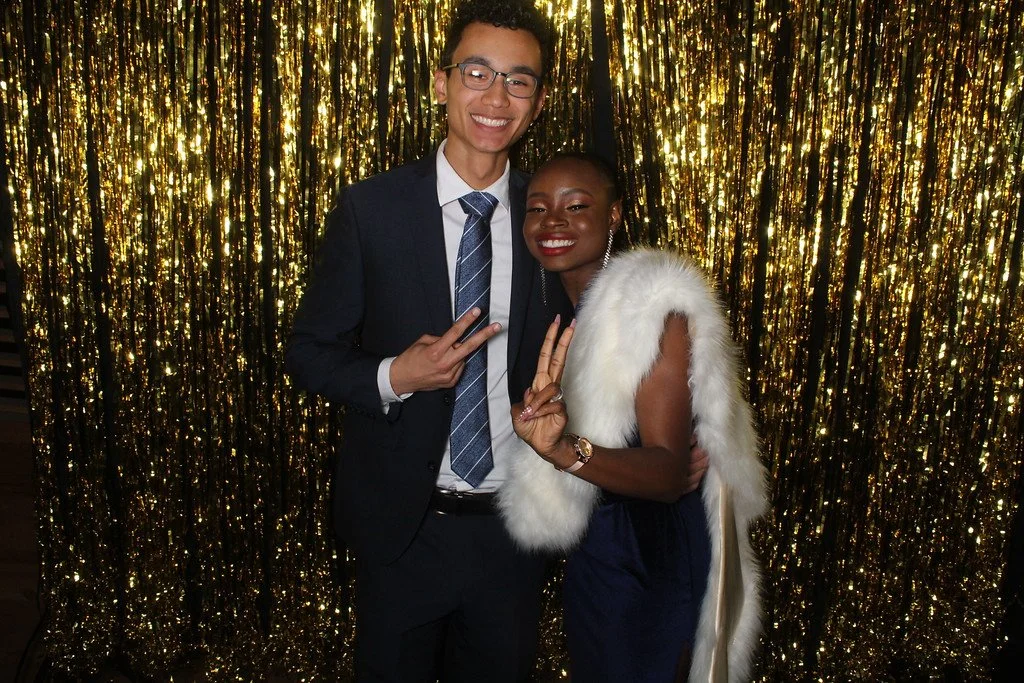 Robert and Mope in formal attire, standing close together in front of a gold glittery backdrop.