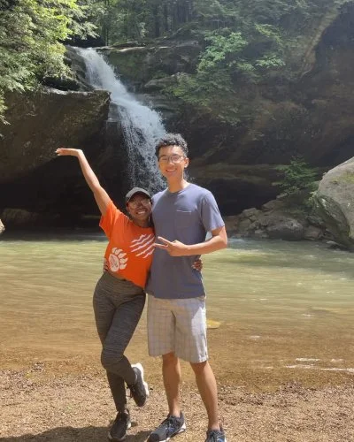 Robert and Mope, smiling and posing by a river with a waterfall and lush green trees in the background.