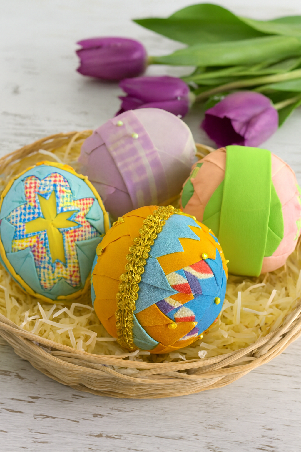 Colorful decorative Easter eggs in a basket with purple tulips in the background.