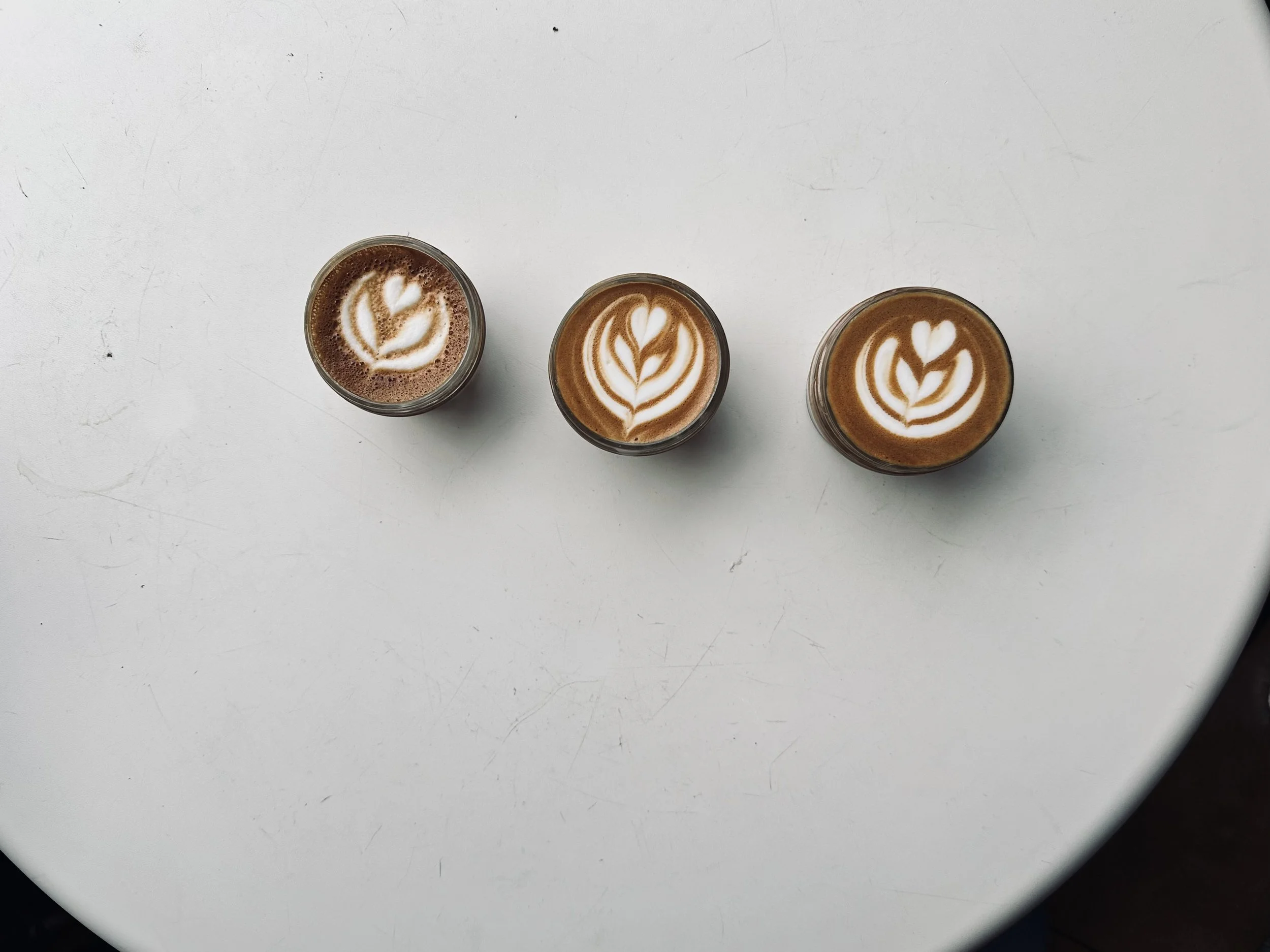 Three coffee drinks with latte art on a white surface.