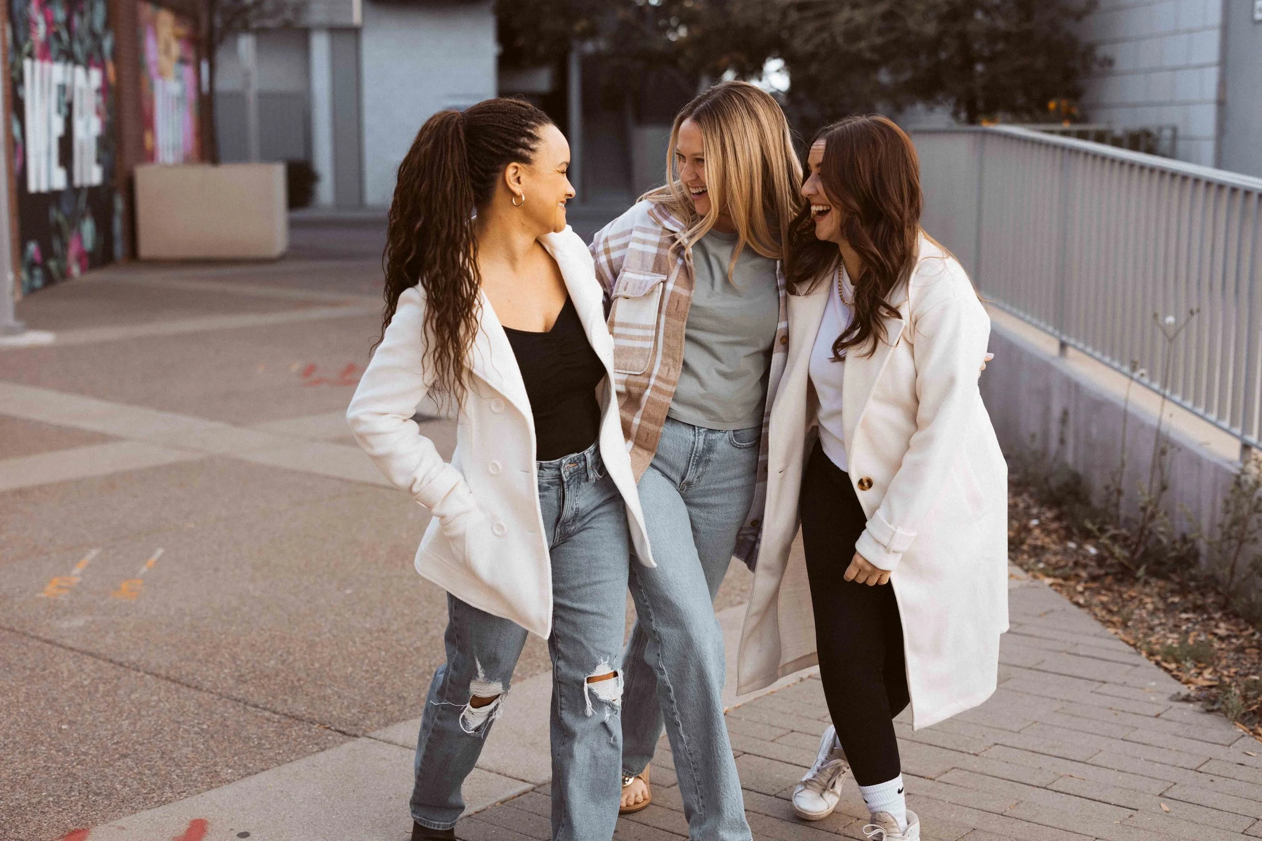Three women standing close together and smiling outside, talking and laughing.