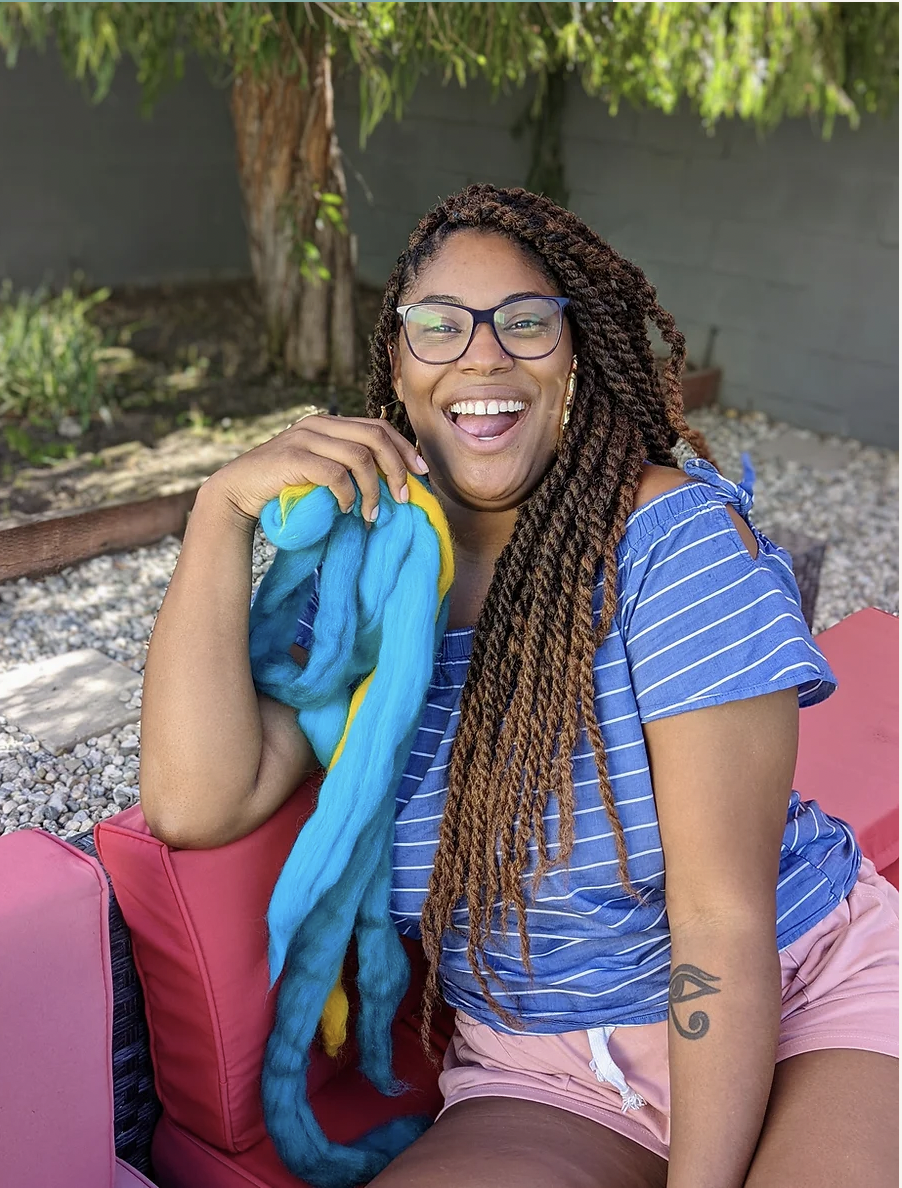 Image of artist Dara M. Wilson sitting on a couch outside smiling at the camera.
