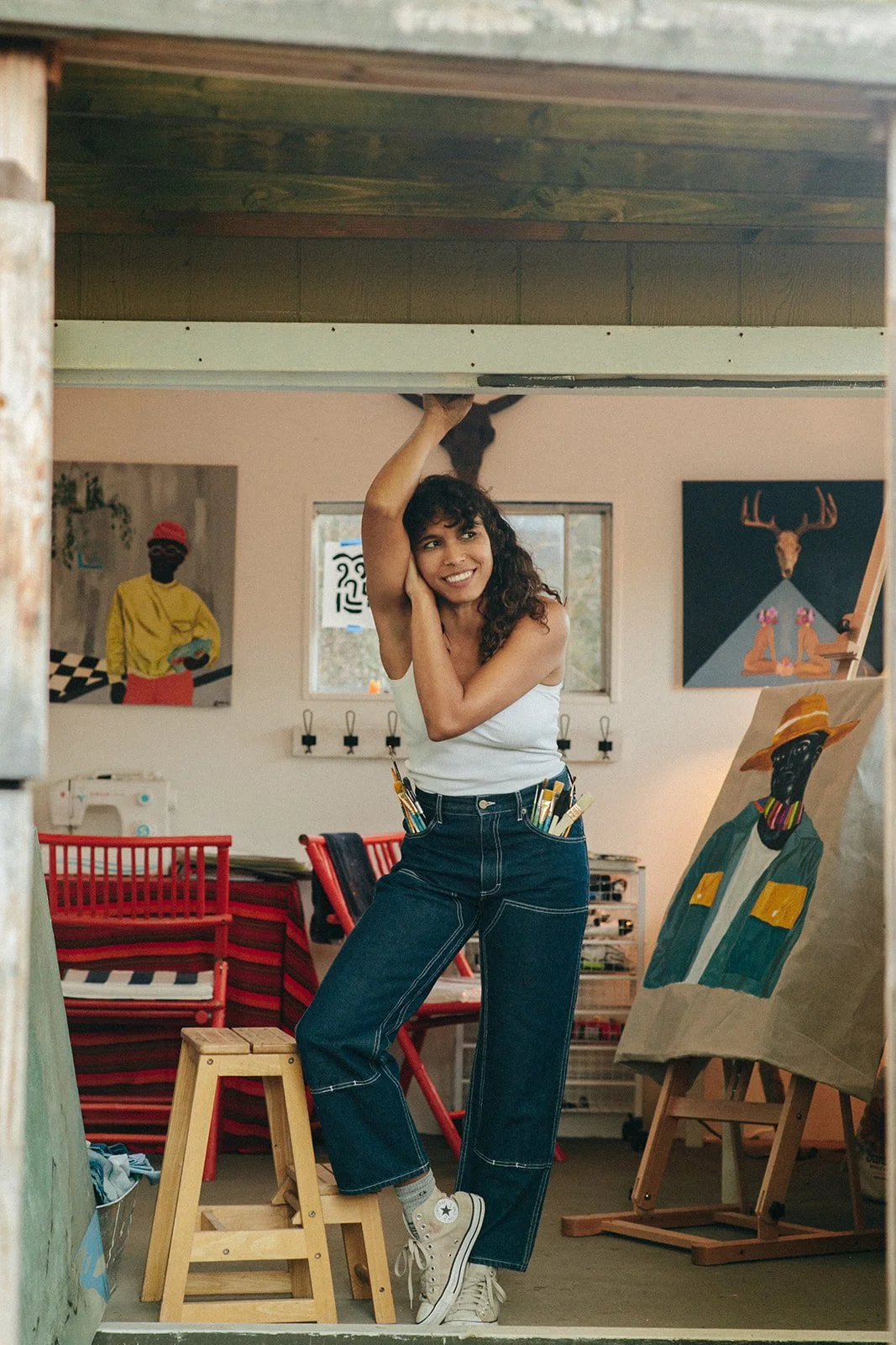 Image of artist Leslie Adkins in her studio facing camera but looking off to the side surrounded by her works.