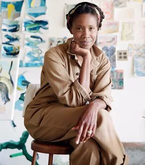 Image of artist K'era Morgan sitting in a stool in her studio surrounded by some of her works. Photo by Lily Glass.