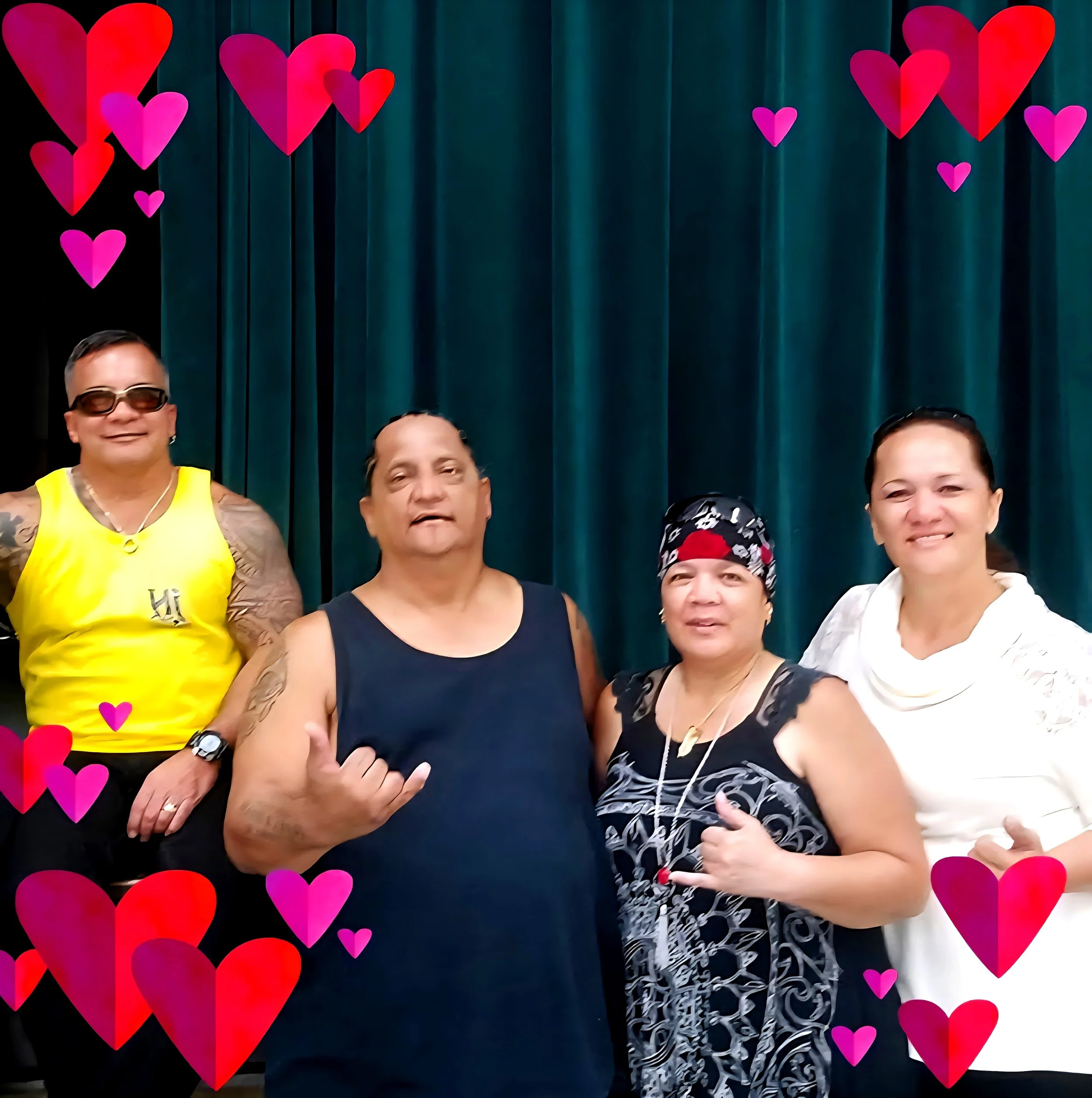Four people standing in front of a blue curtain with heart decorations around the border, smiling and posing for the camera.
