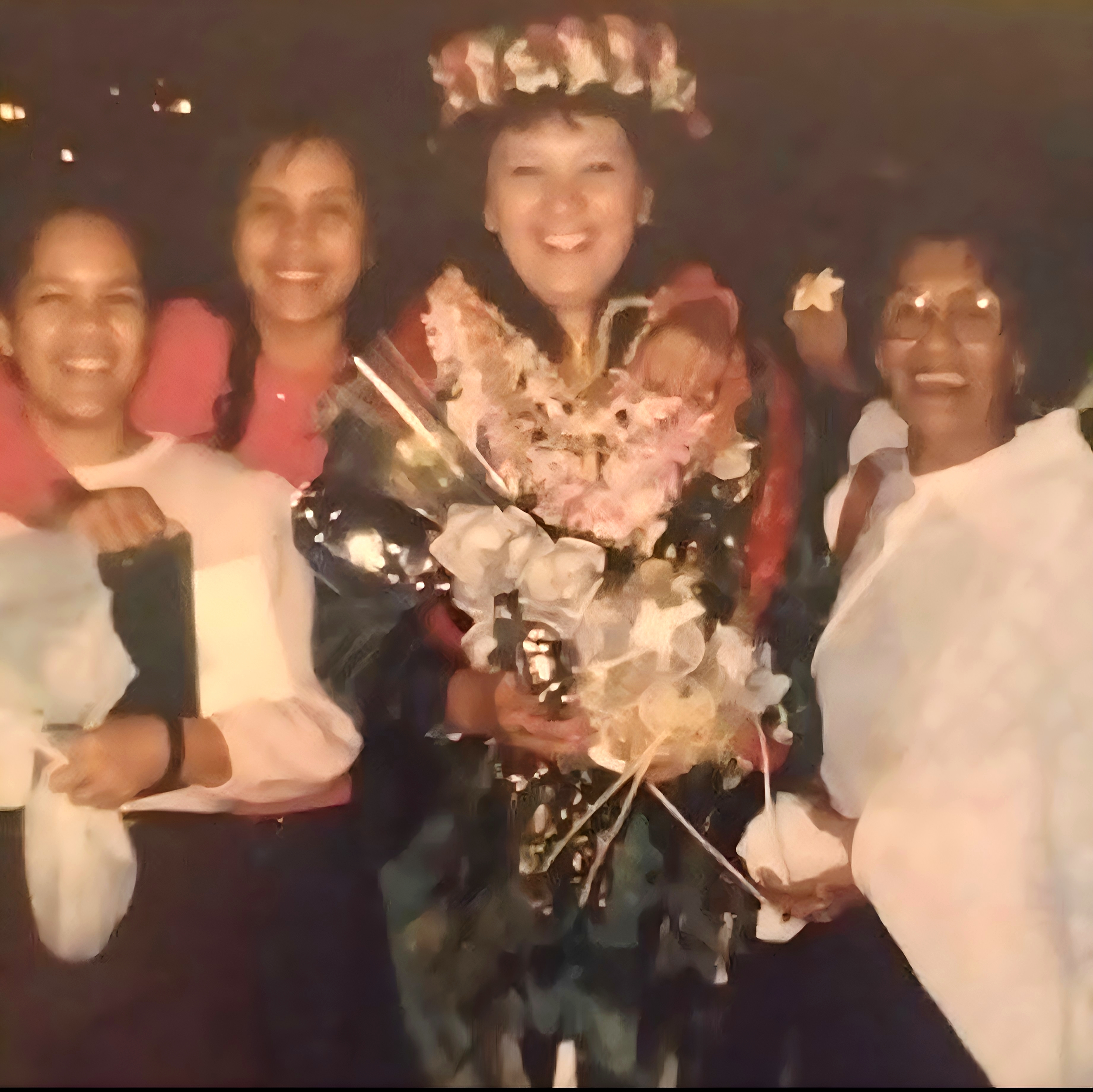 Group of four women smiling, one holding a bouquet of flowers, celebrating at night.