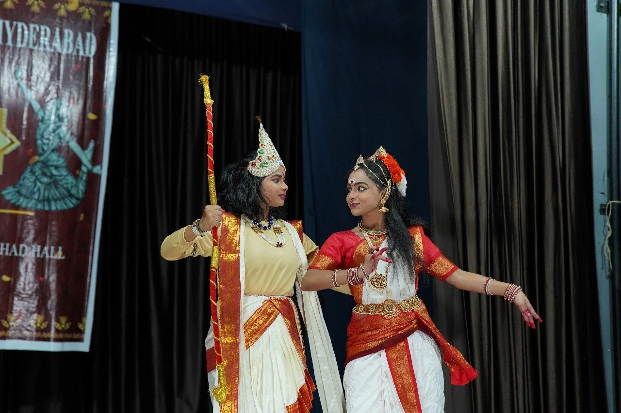 Two women dressed in traditional Indian attire performing on stage during a cultural event.