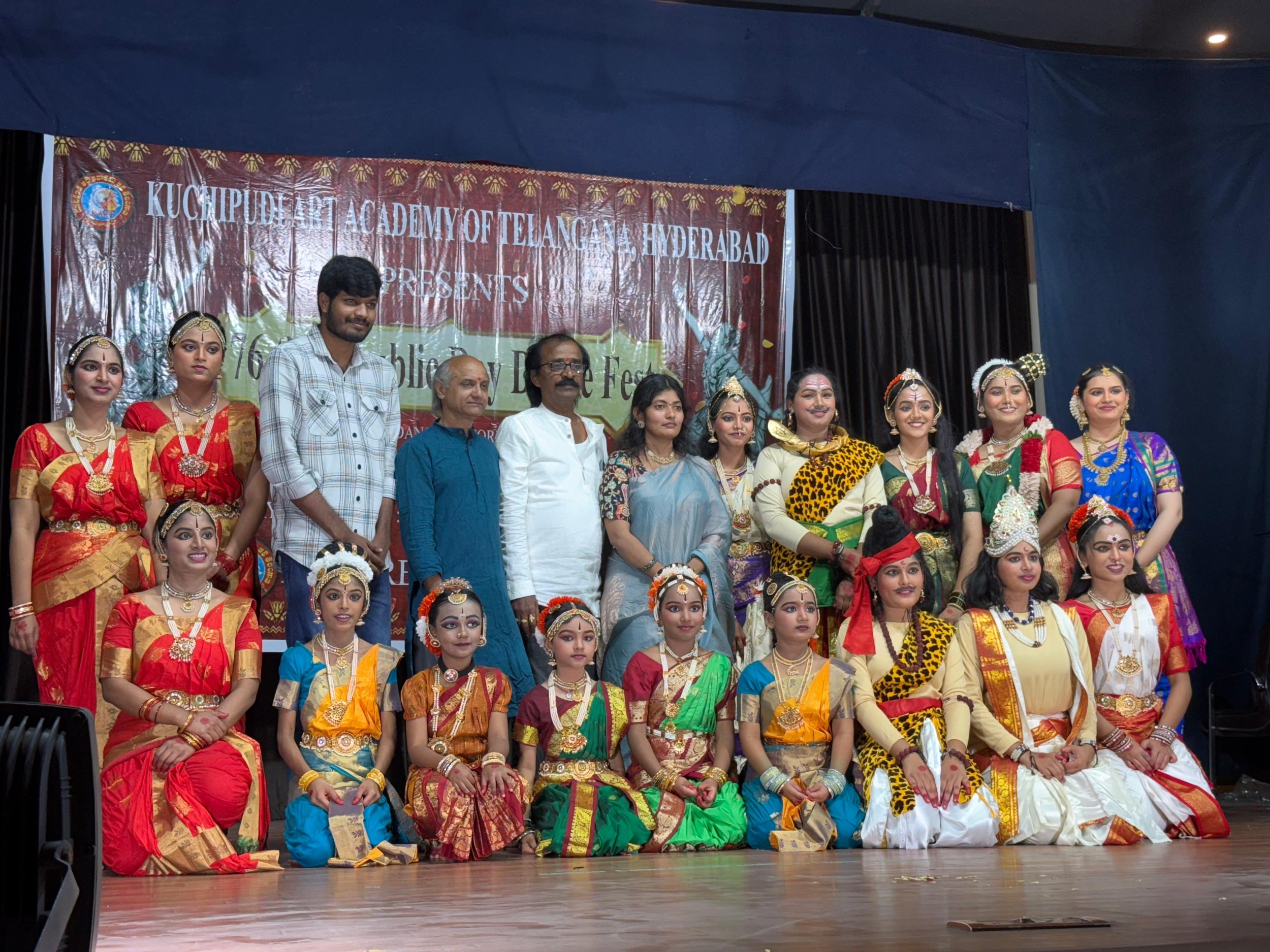 Group photo of children and adults dressed in traditional Indian clothing on stage during a cultural event.