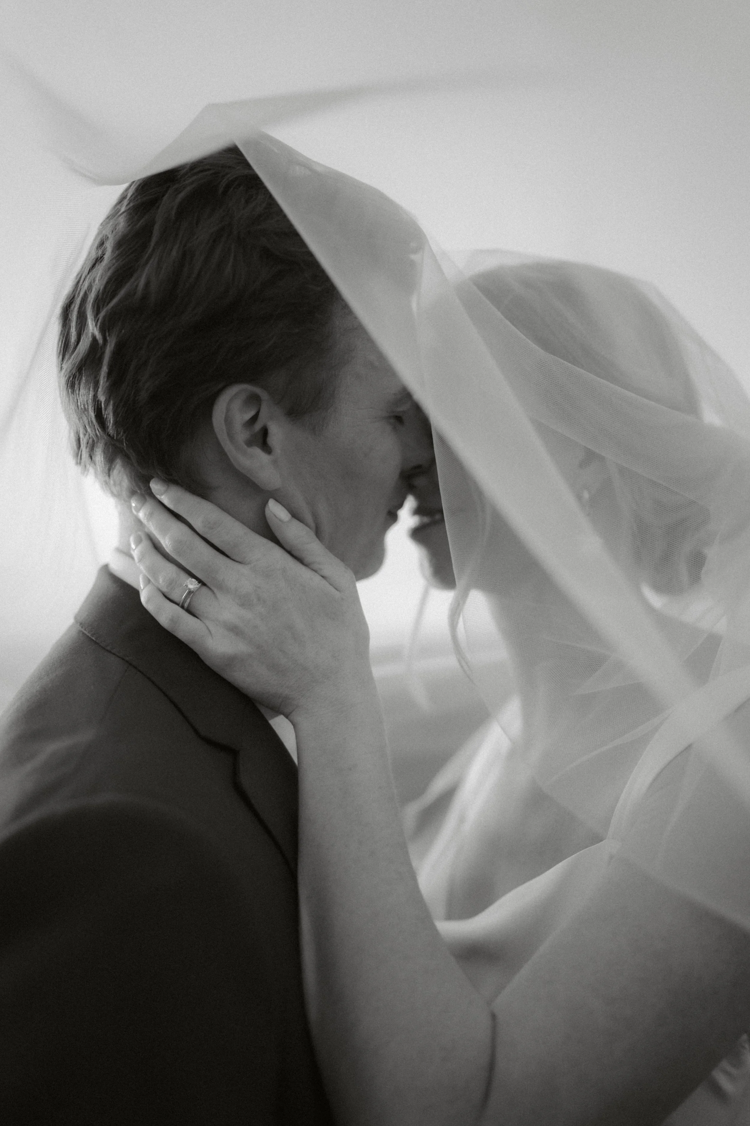 A woman and a man share a kiss under a sheer fabric, with the woman's hand gently touching the man's face.