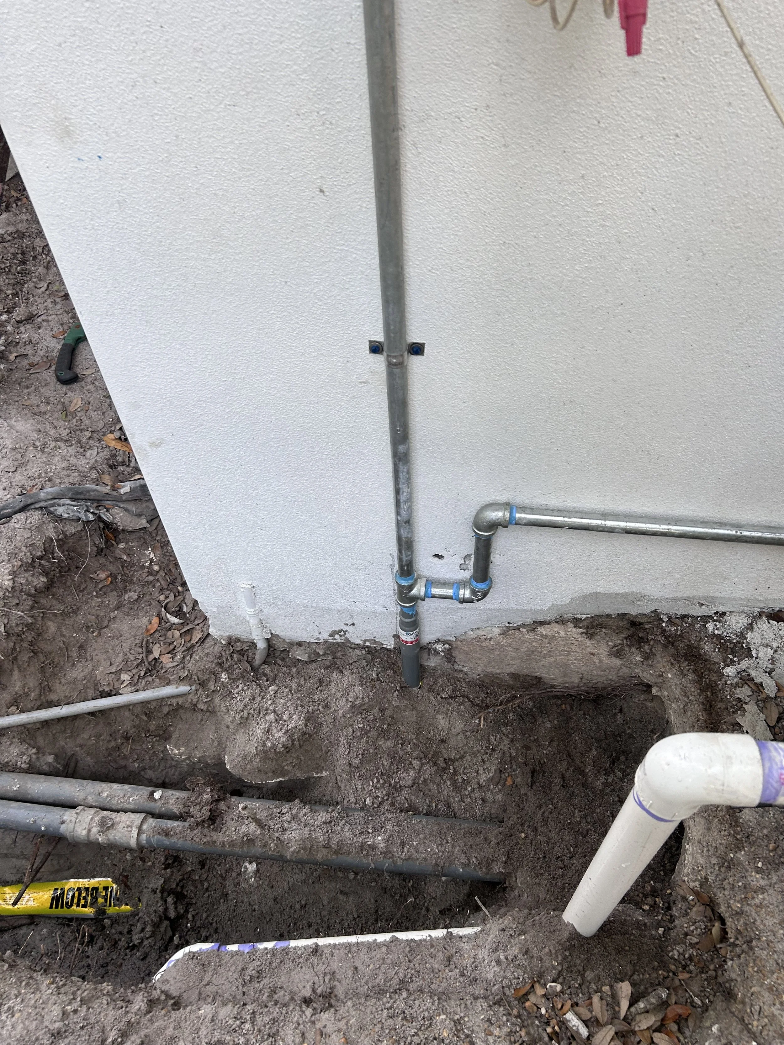 Installation of plumbing pipes on a wall, with exposed pipes protruding from the ground and running along the wall, in a construction or renovation site.
