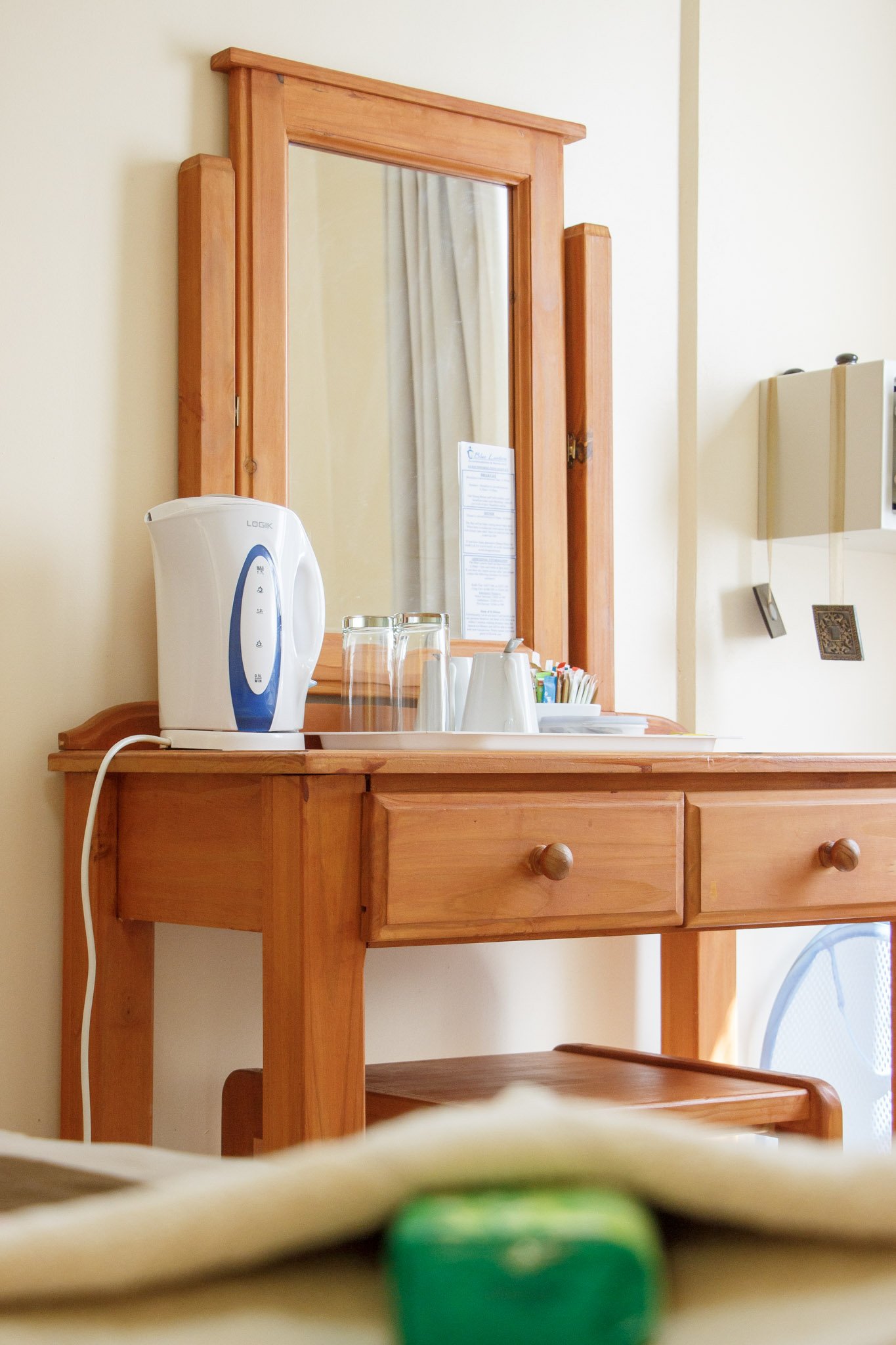 Wooden dresser with a mirror, electric kettle, glasses, cups, and small packets on the top.