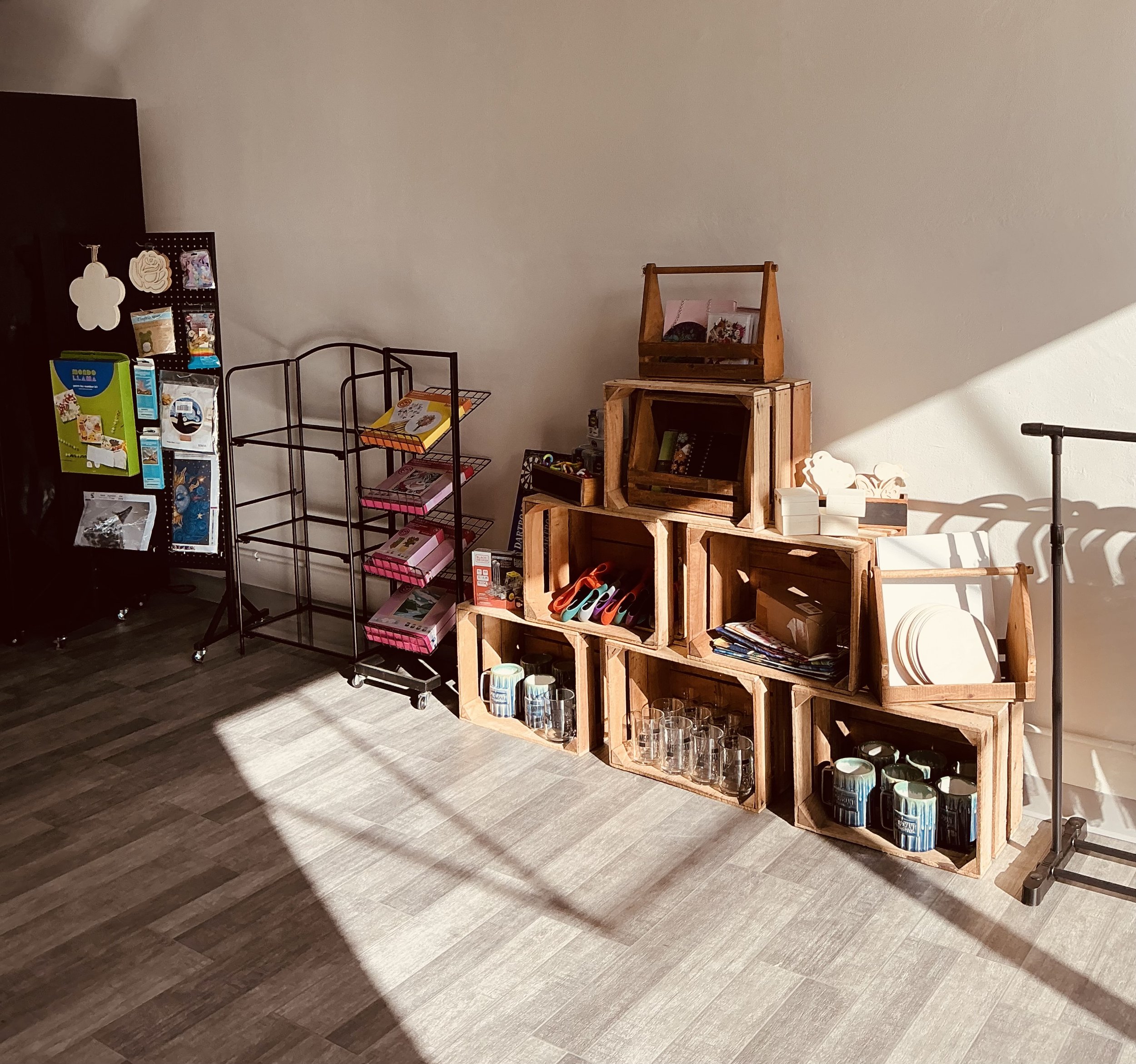 Display of wooden crates, glassware, and kitchen items arranged on the wall, next to black metal racks with various items, all illuminated by sunlight.