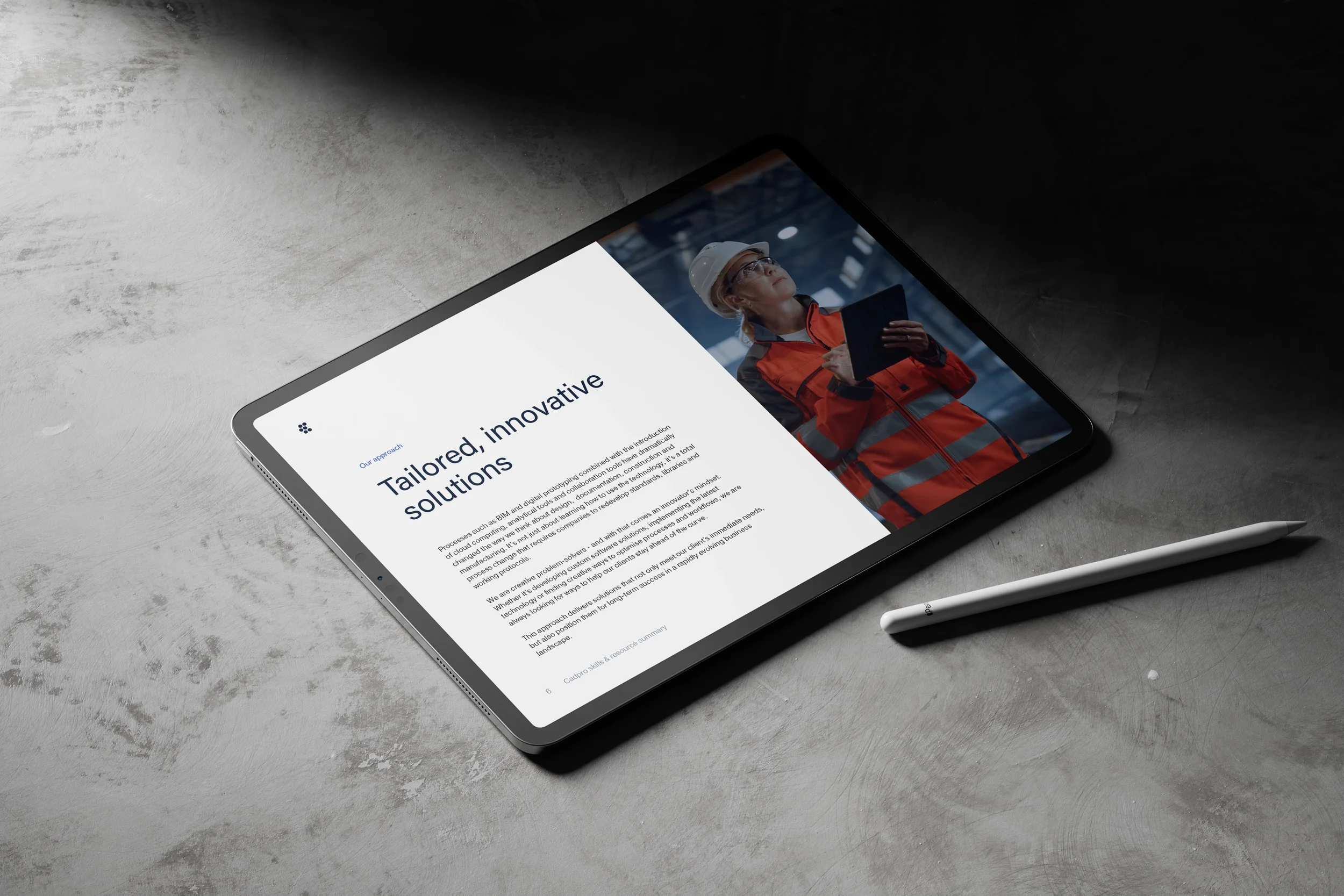 A tablet displaying a webpage with text titled "Tailored, innovative solutions" and an image of a woman in safety gear holding a clipboard in an industrial setting. The tablet is on a concrete surface next to a white stylus pen.