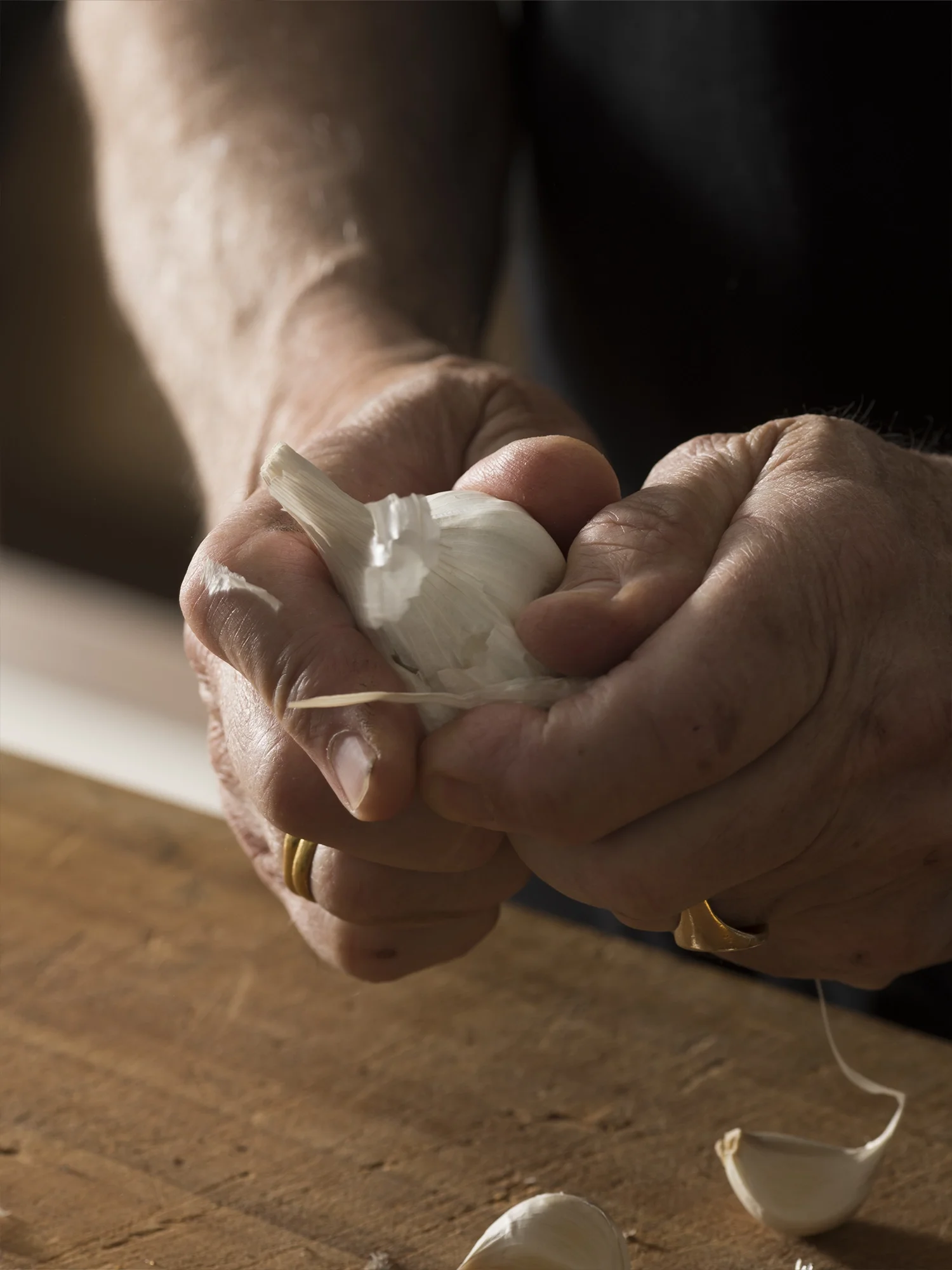 Hands peeling garlic above a wooden surface.
