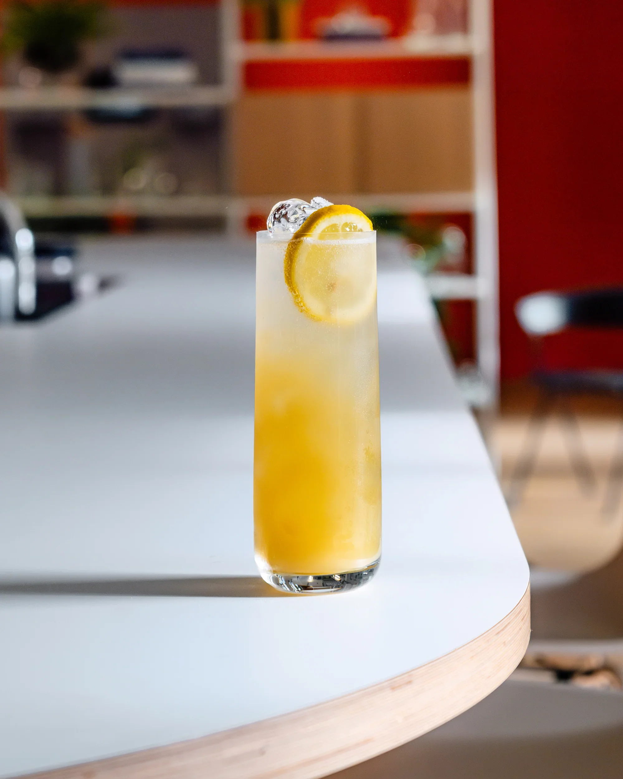 A tall glass of lemonade with ice and lemon slices on a white surface in a modern indoor setting.