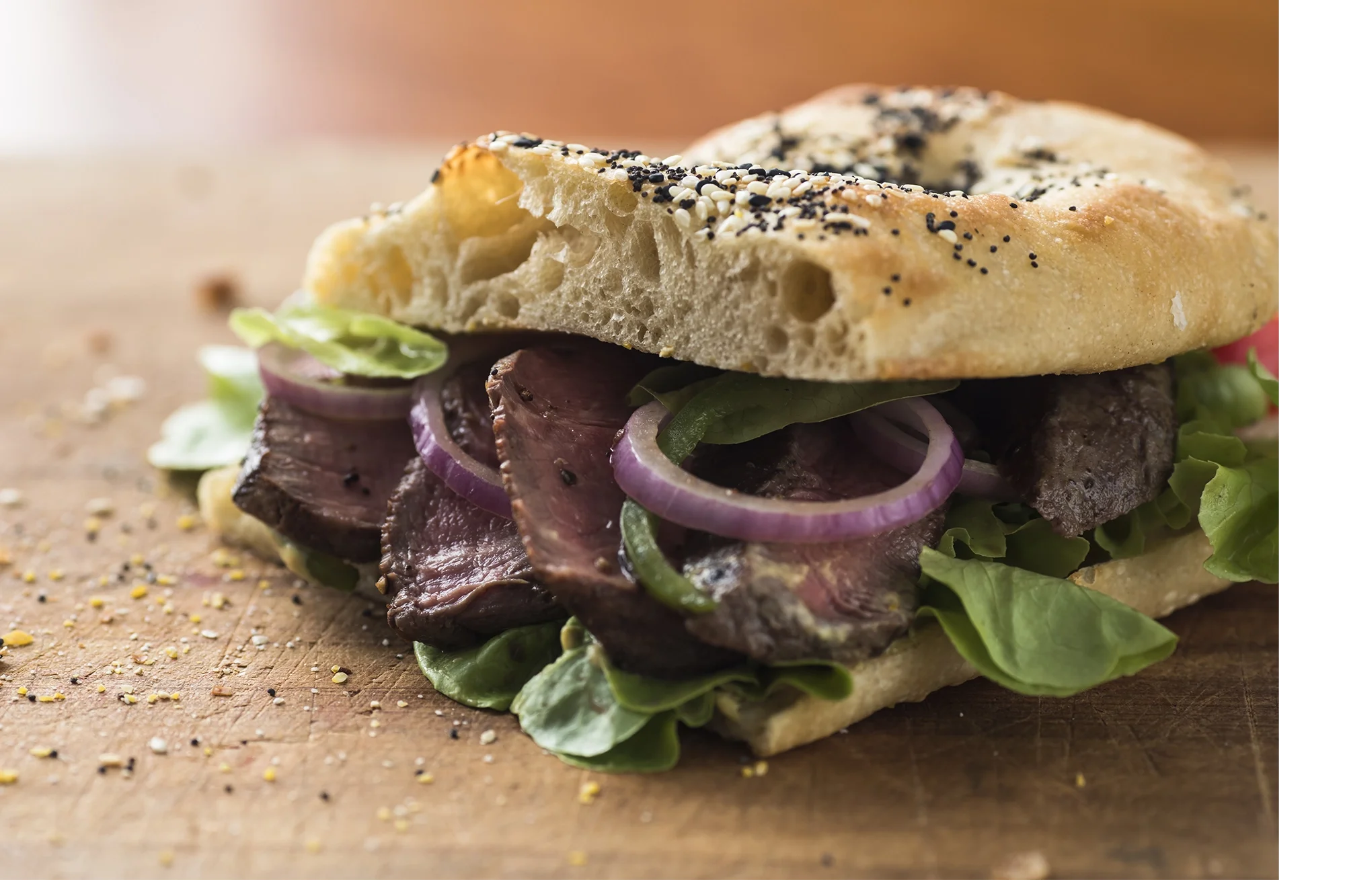 Close-up of an i sandwich with cooked beef, red onion slices, lettuce, on a wooden surface.
