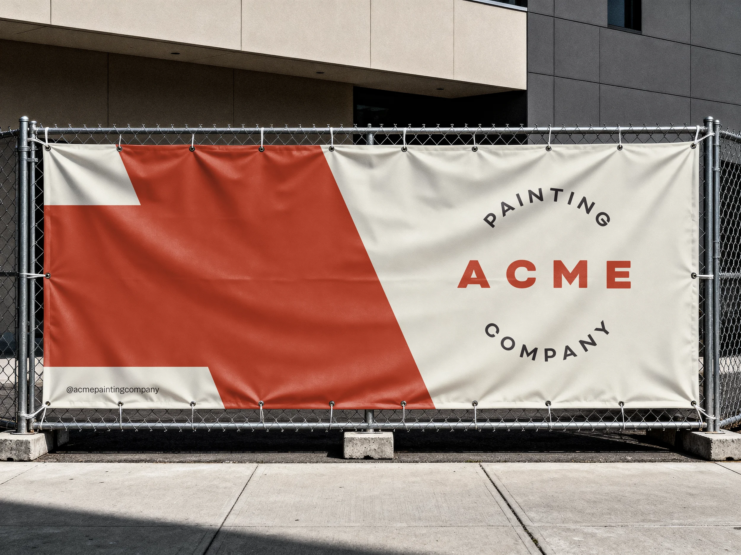 A large banner advertising ACME painting company, with red and white geometric design, mounted on a chain-link fence.