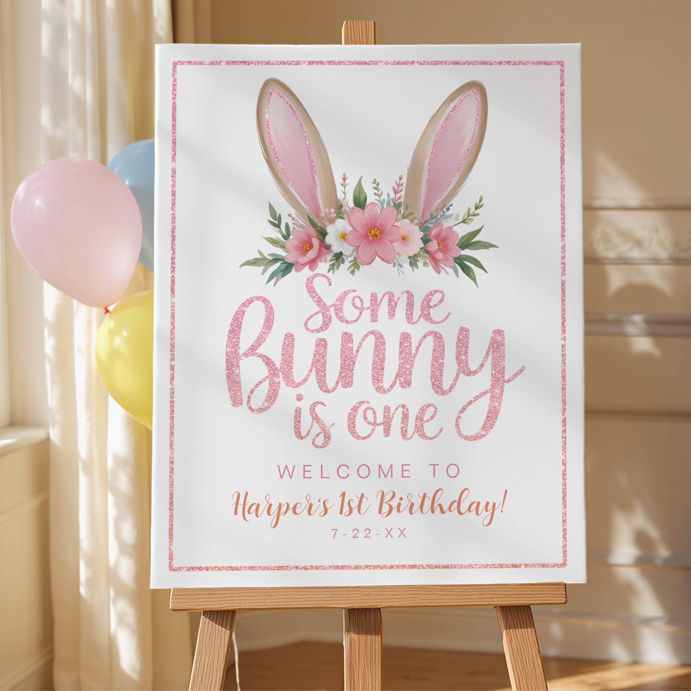 Some Bunny Is One welcome sign featuring pink glitter script and floral bunny ears displayed on an easel with balloons.