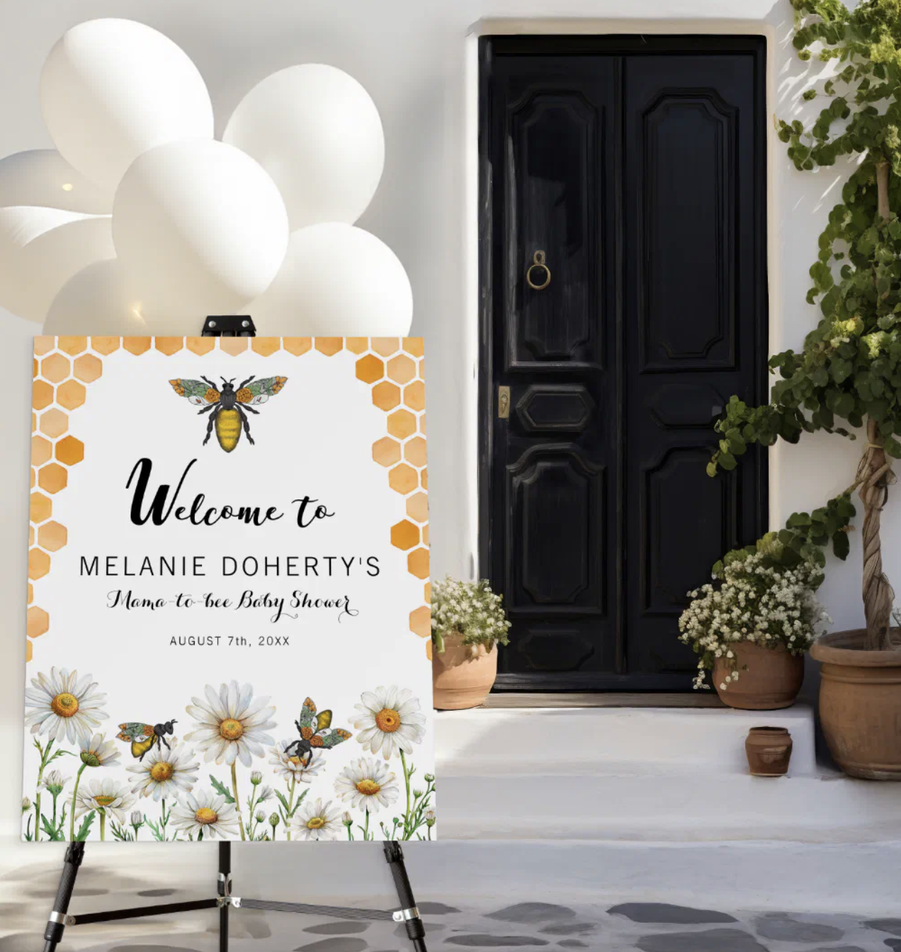 Honey bee baby shower welcome sign with daisies and honeycomb design displayed on an easel at the entrance of a garden baby shower