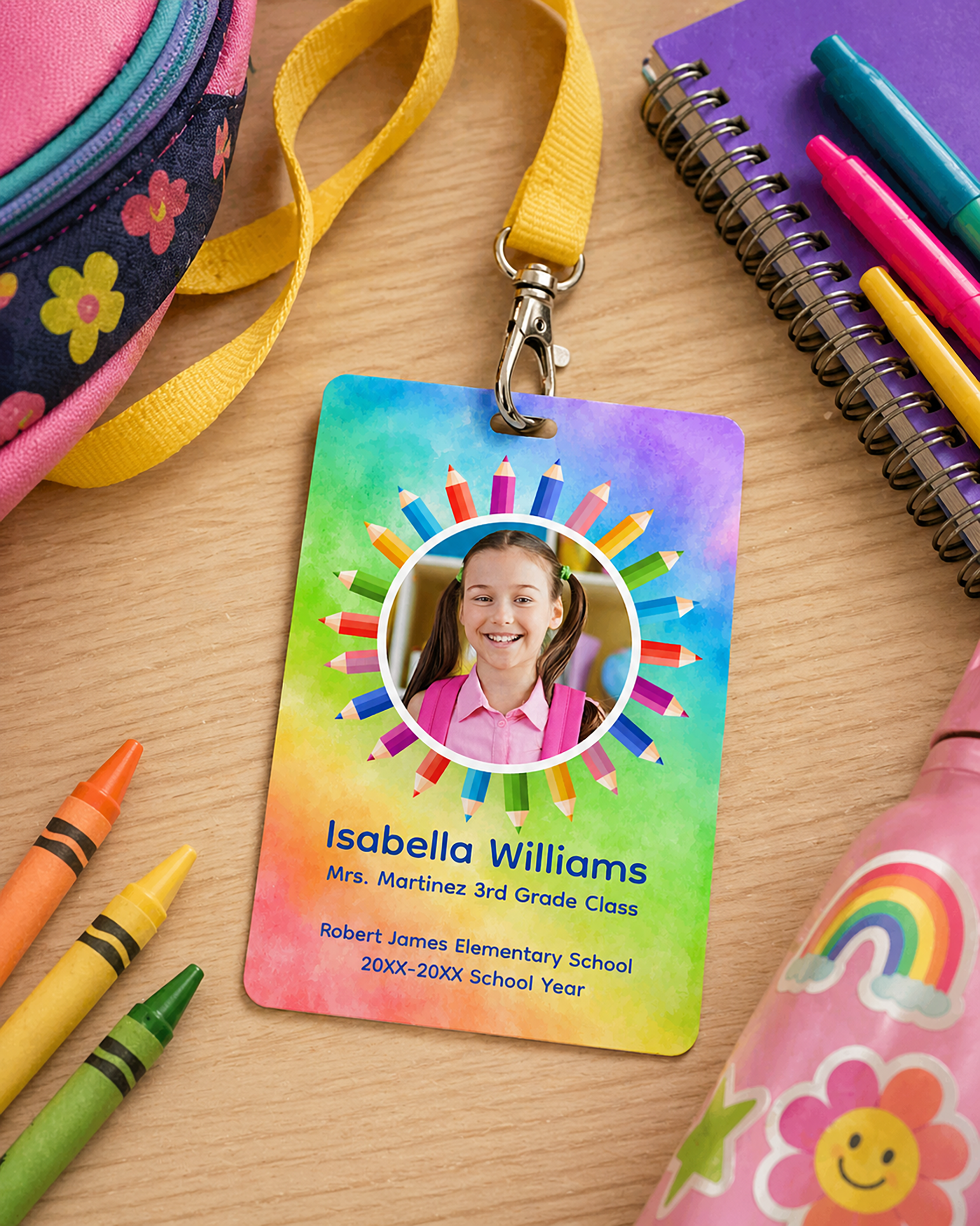 Rainbow personalized student ID badge with a child photo on a yellow lanyard placed on a wooden desk with crayons, notebook, backpack, and colorful school supplies.