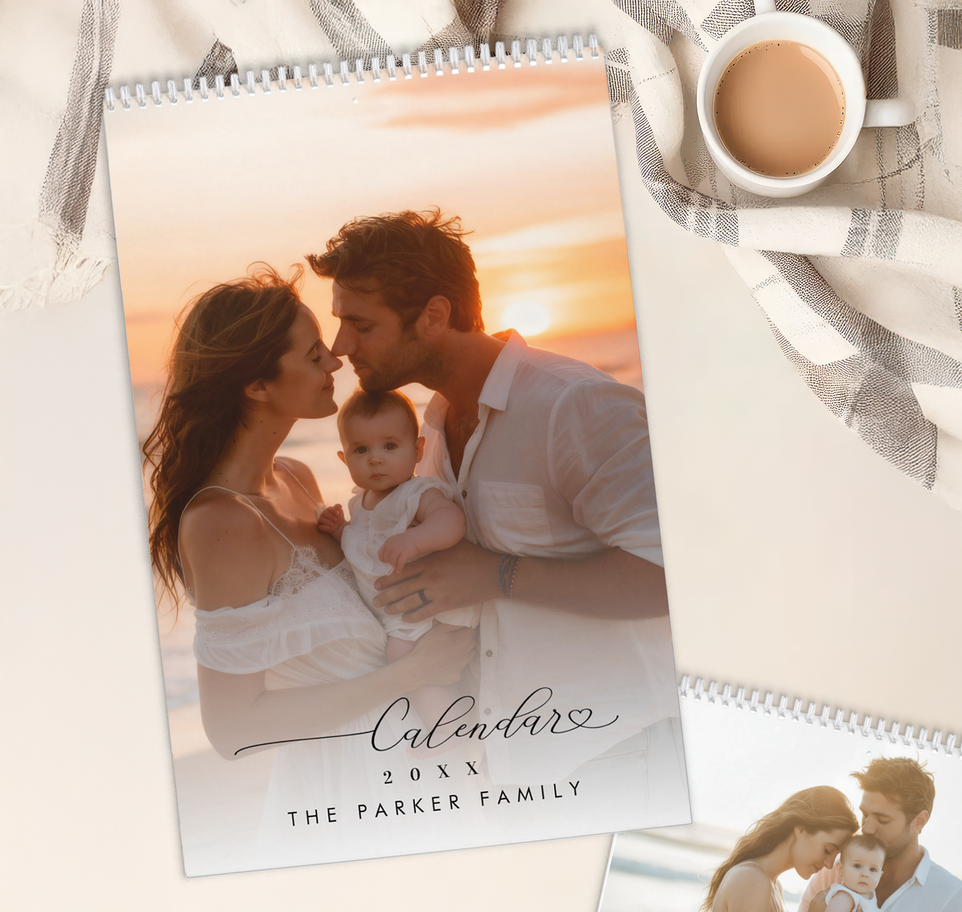 Personalized family photo wall calendar featuring a sunset beach portrait of parents holding their baby, displayed on a neutral tabletop beside a coffee cup and folded linen cloth.