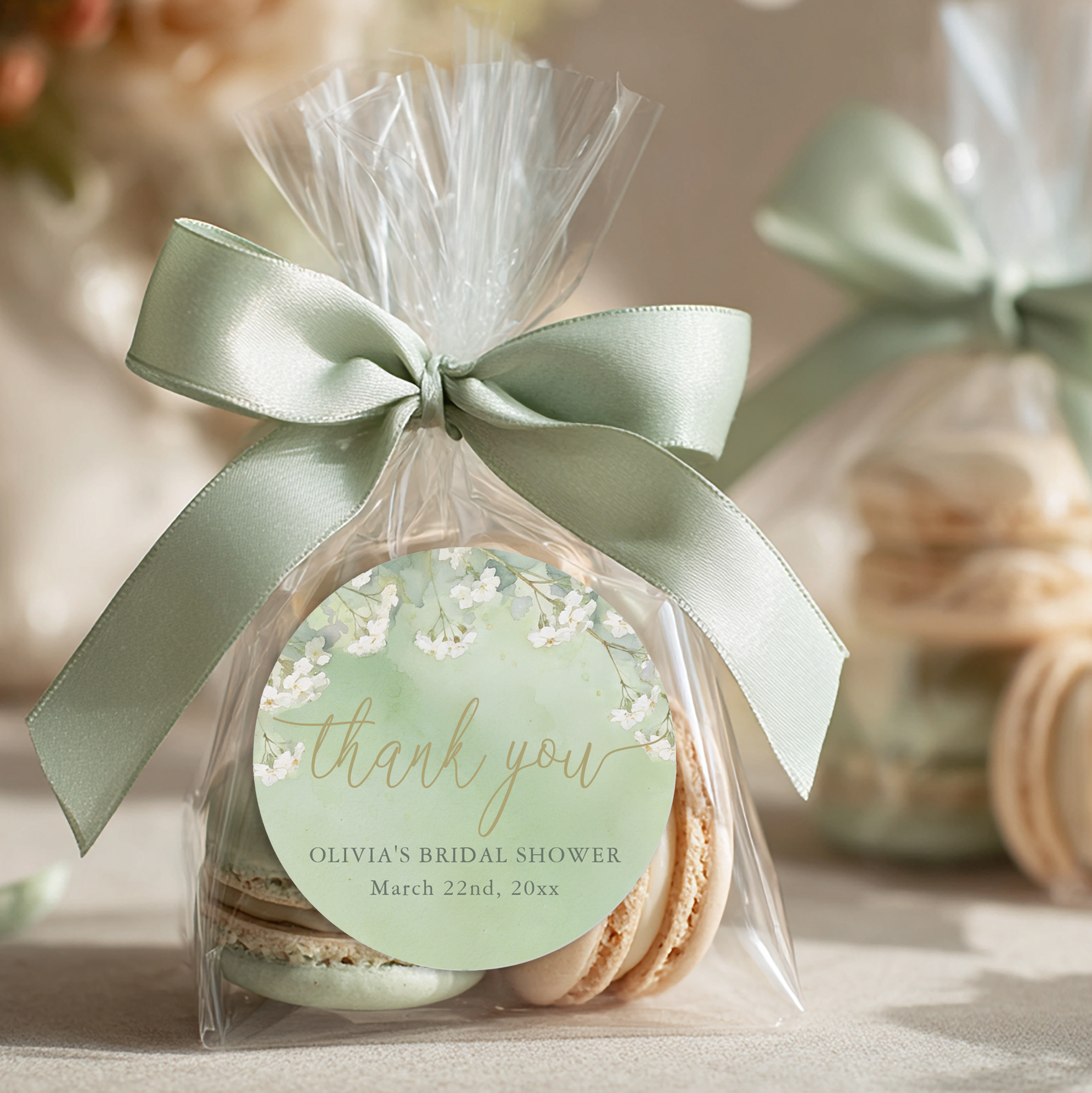 Sage green floral bridal shower thank you favor sticker on a clear treat bag tied with a satin ribbon, styled with macarons.