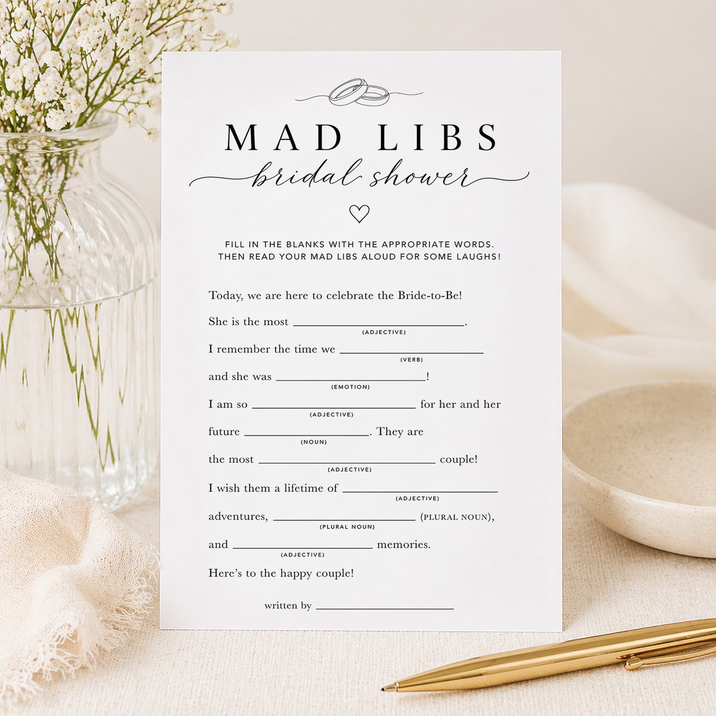 Elegant Bridal Shower Mad Libs game card displayed in a soft neutral flat lay with white florals, gold pen, linen fabric, and minimalist styling. Printable-style bridal shower word game with black and white typography for a modern bridal celebration.