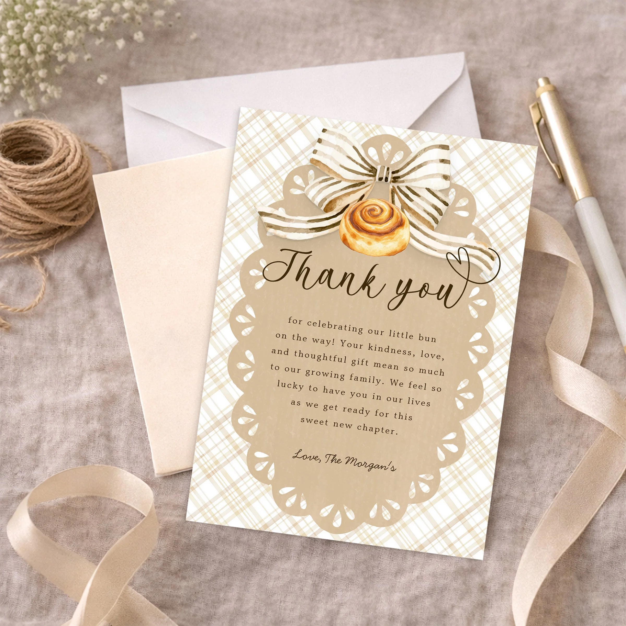 Bun in the Oven baby shower thank you card with neutral gingham design, displayed with envelope, ribbon, twine, and pen on soft fabric background.