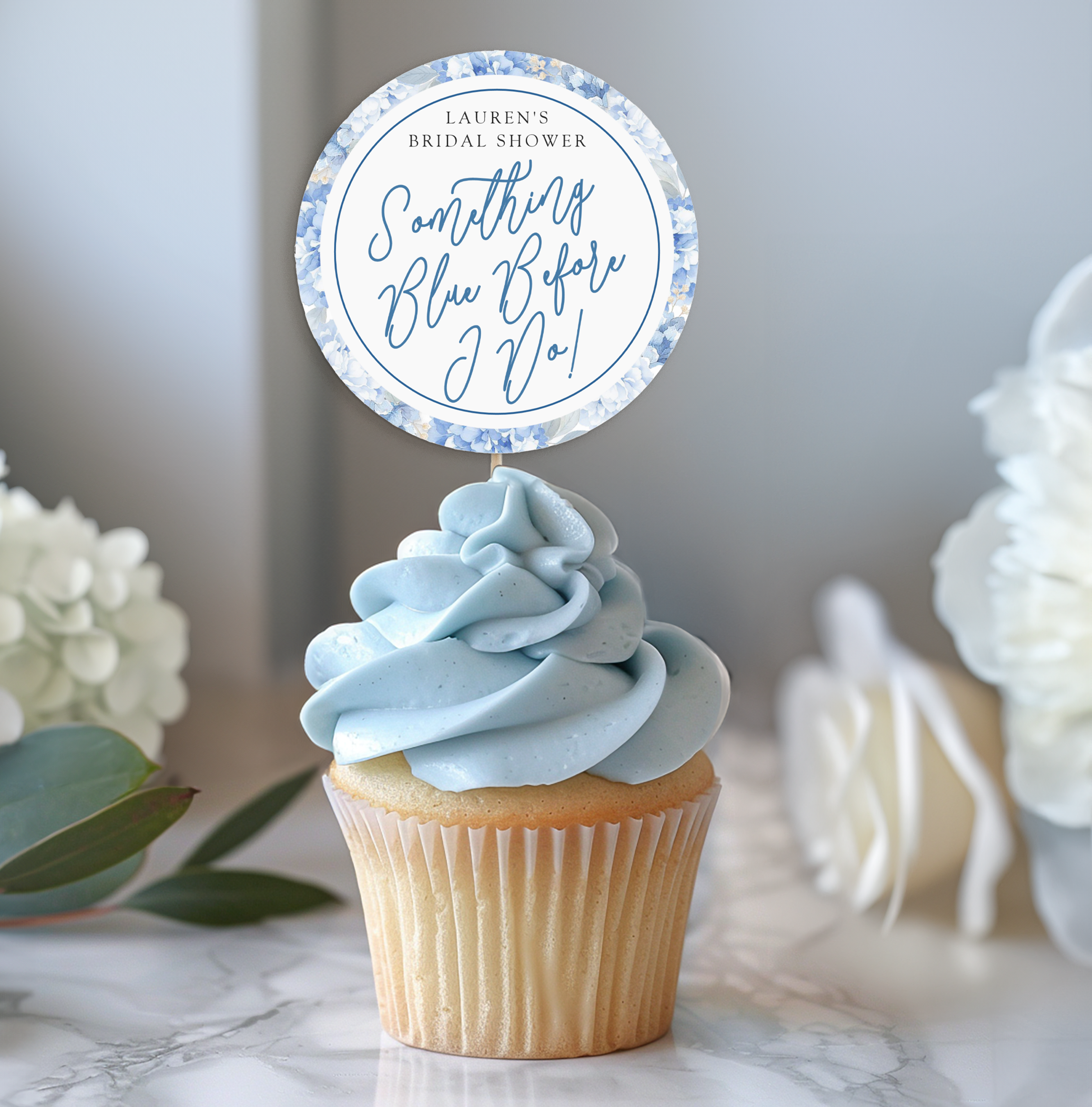 Round bridal shower favor sticker reading “Something Blue Before I Do” displayed on a cupcake with soft blue frosting.