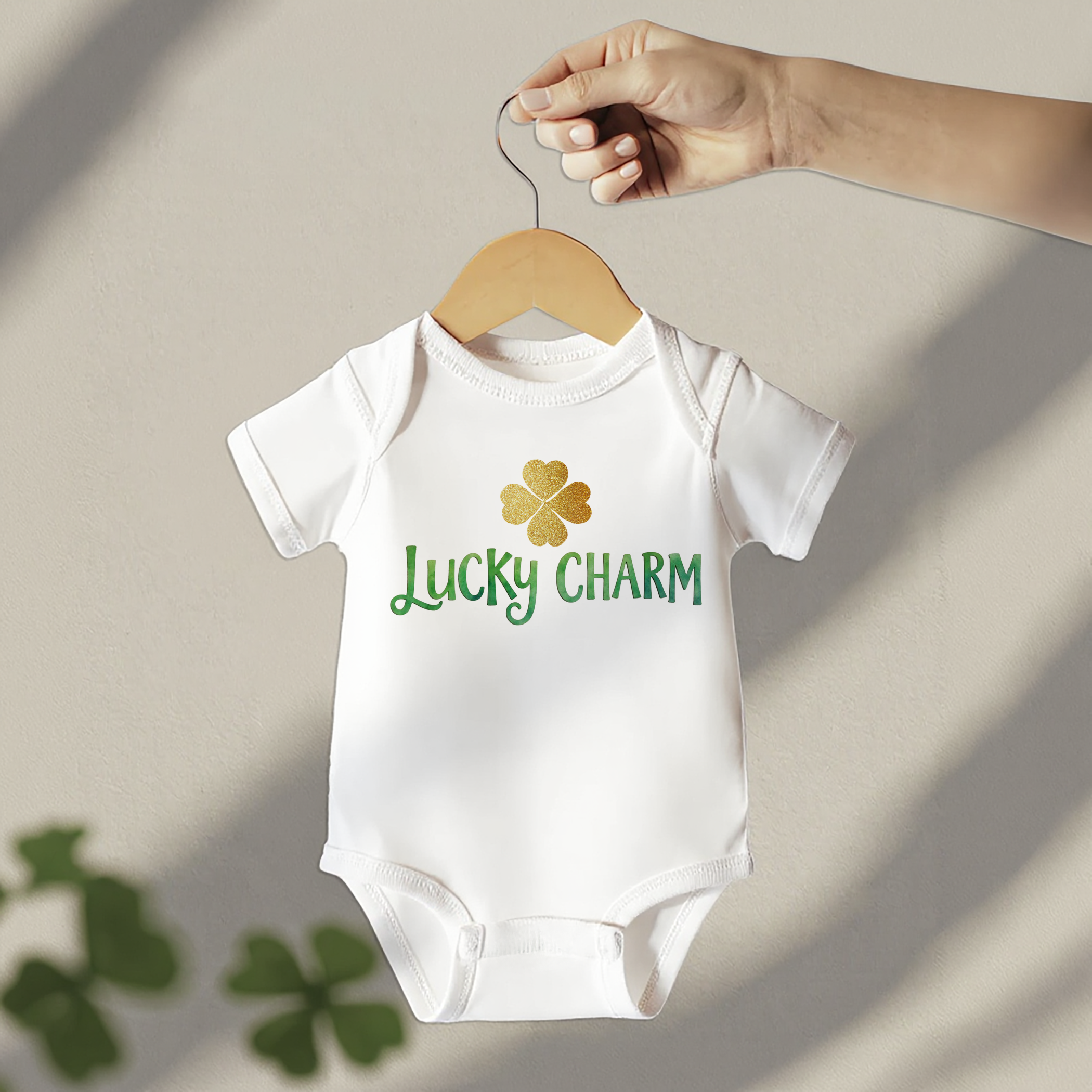 Lucky Charm baby onesie with green lettering and a gold clover accent, styled on a festive green background for a Lucky Charm baby shower theme.