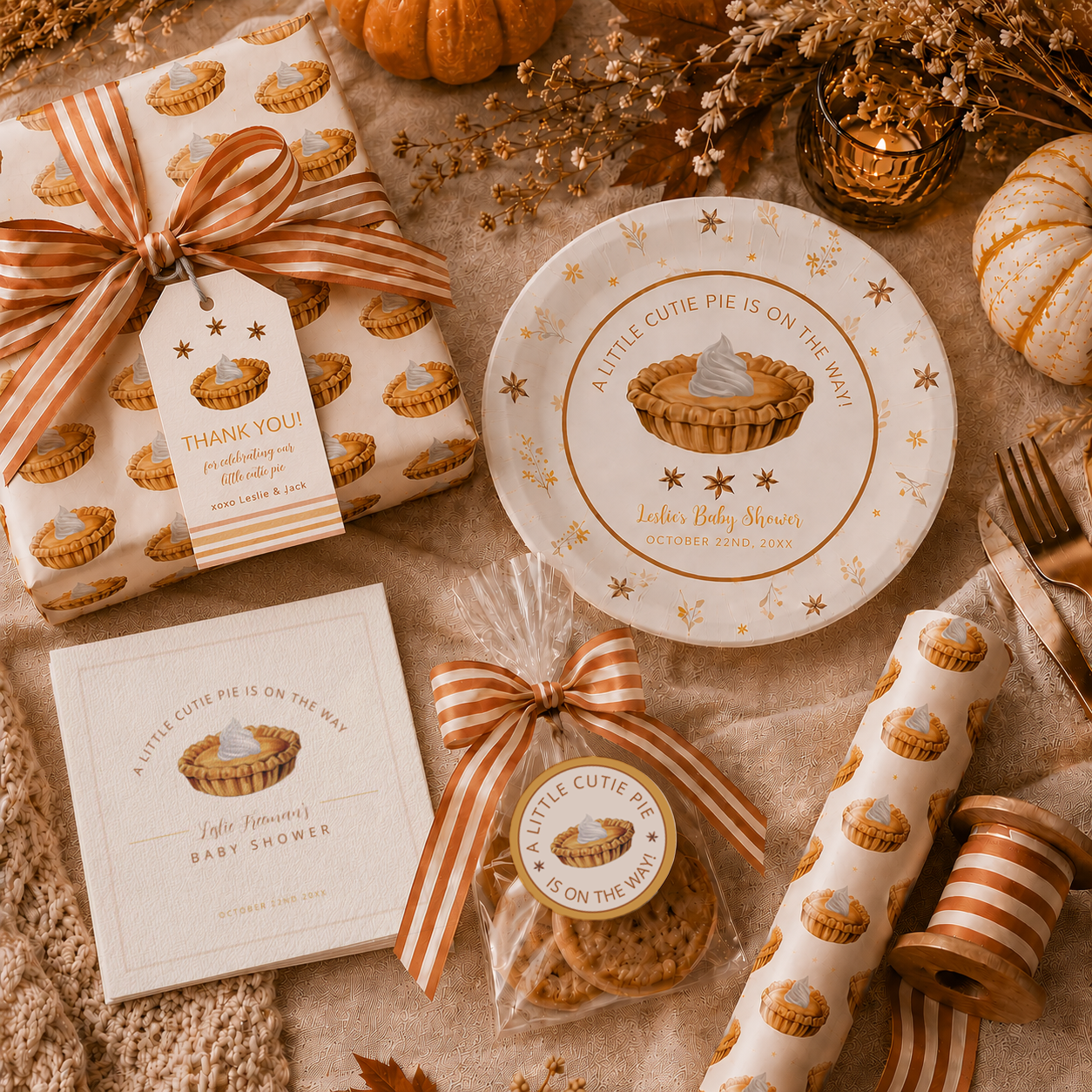 Autumn-inspired baby shower flat lay featuring pie-themed wrapping paper, striped ribbon, personalized paper plates, white cocktail napkins, cookie favors with round stickers, and cozy fall decor in warm neutral and pumpkin spice tones.