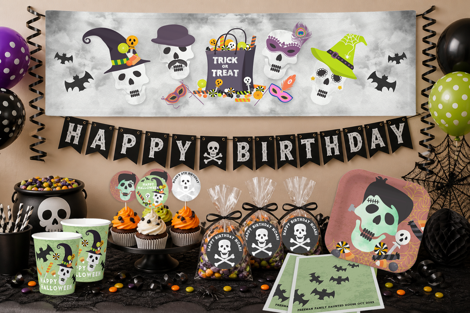 Halloween birthday party table styled with a large decorative banner, black “Happy Birthday” garland, themed plates, cups, napkins, cupcakes, and candy favor bags arranged in a festive display.