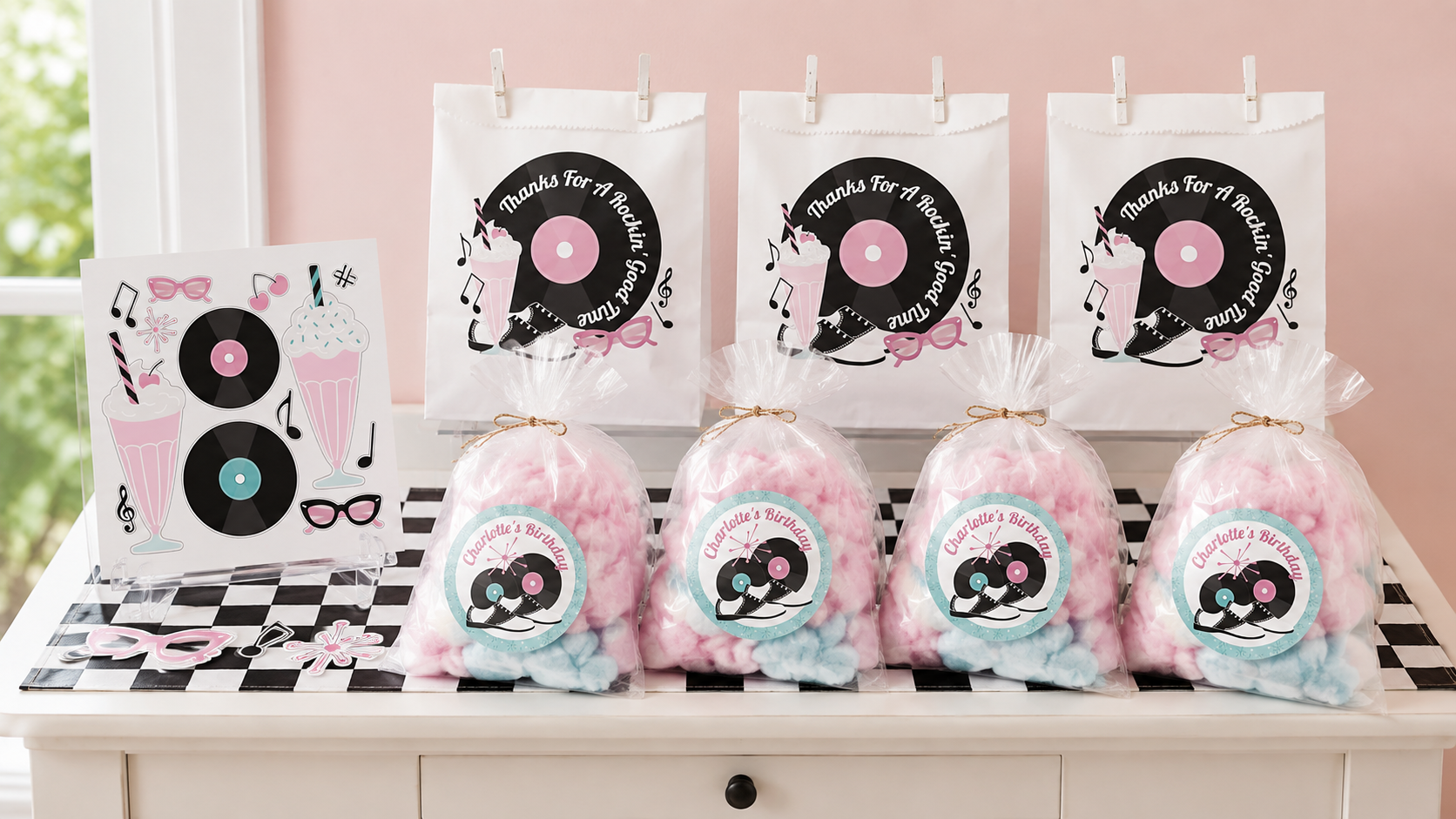 1950s sock hop favor display with retro sticker sheets, personalized paper bags, and pink, aqua, and white cotton-candy favors.