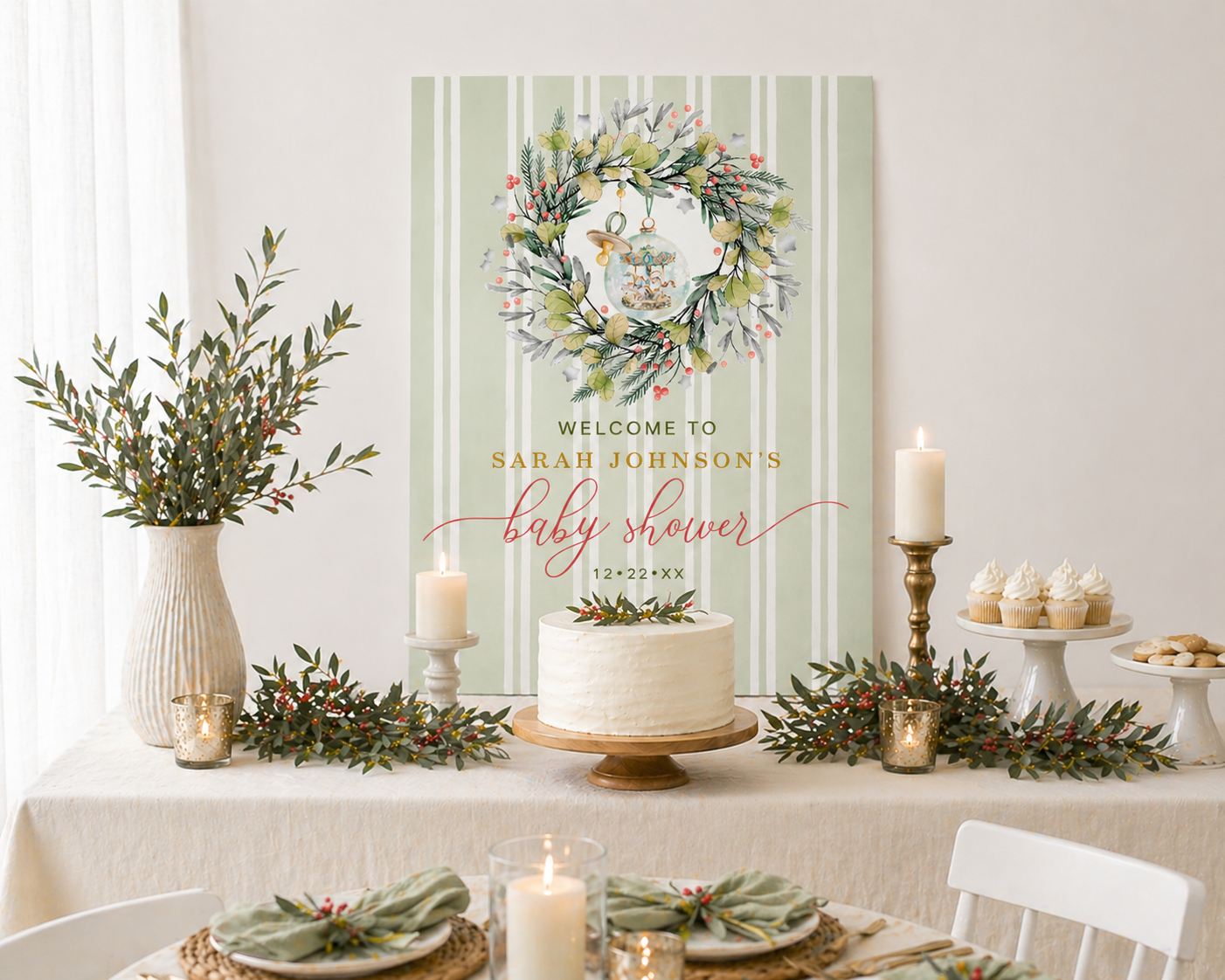 Elegant Christmas baby shower dessert table styled with cream linens, white frosted cake, candles, greenery garlands with subtle red berries, cupcakes, and a custom sage green striped welcome sign featuring a holiday wreath design.