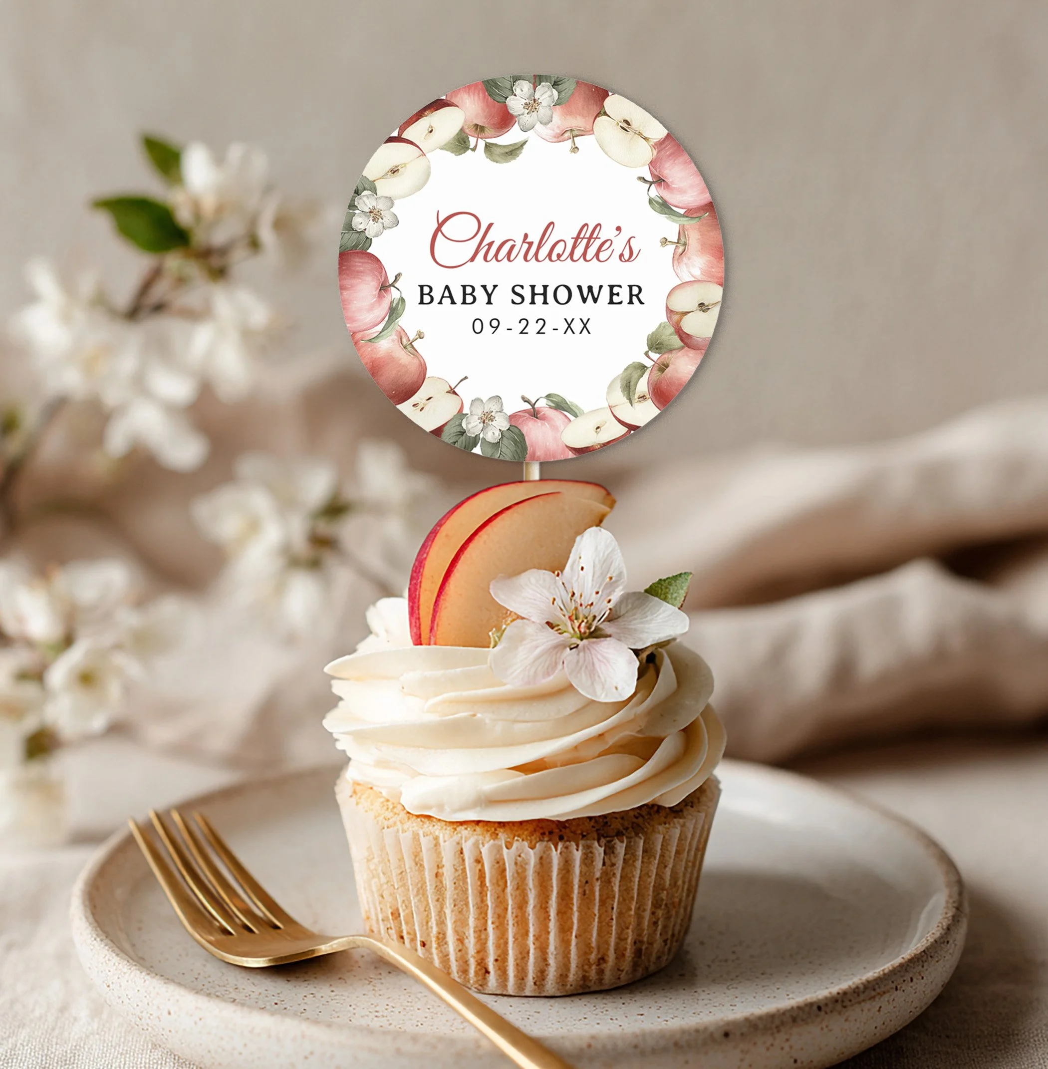 Apple of Our Eye baby shower cupcake topped with personalized apple-themed cupcake topper, apple slice garnish, white blossom flower, and rustic dessert styling.