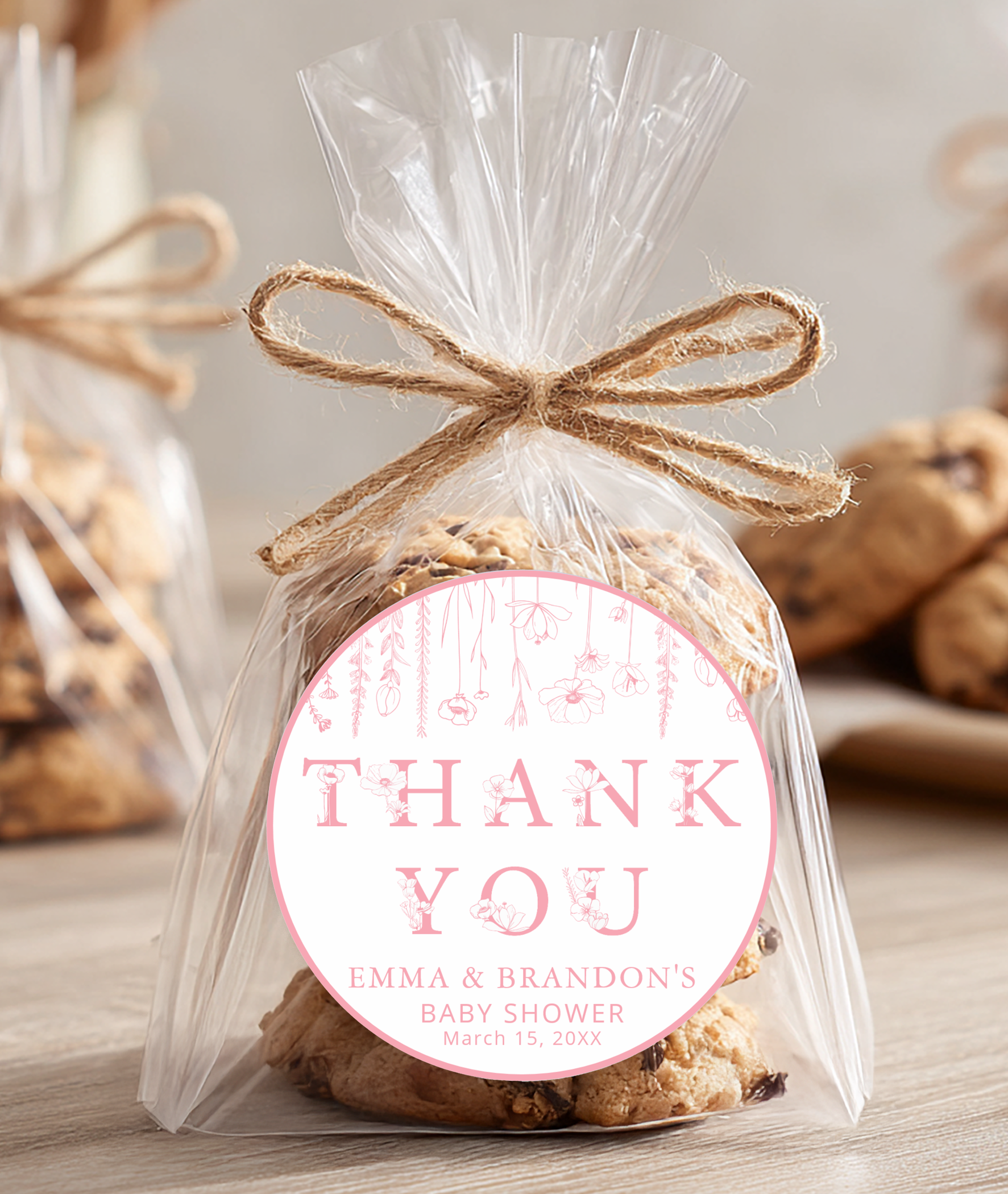Dusty pink wildflower baby shower favor with thank you sticker on wrapped cookies tied with twine in a soft rustic setting