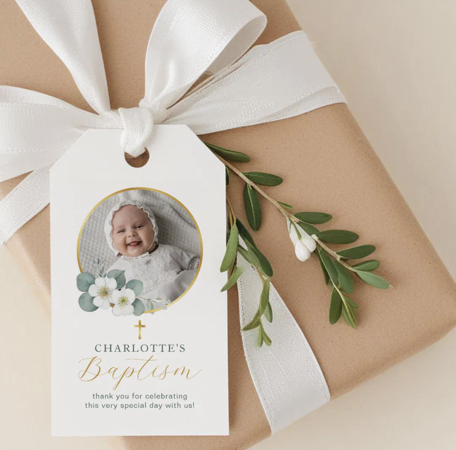 Personalized baptism gift tag with baby photo, gold script text, and delicate greenery accents tied onto a wrapped gift.