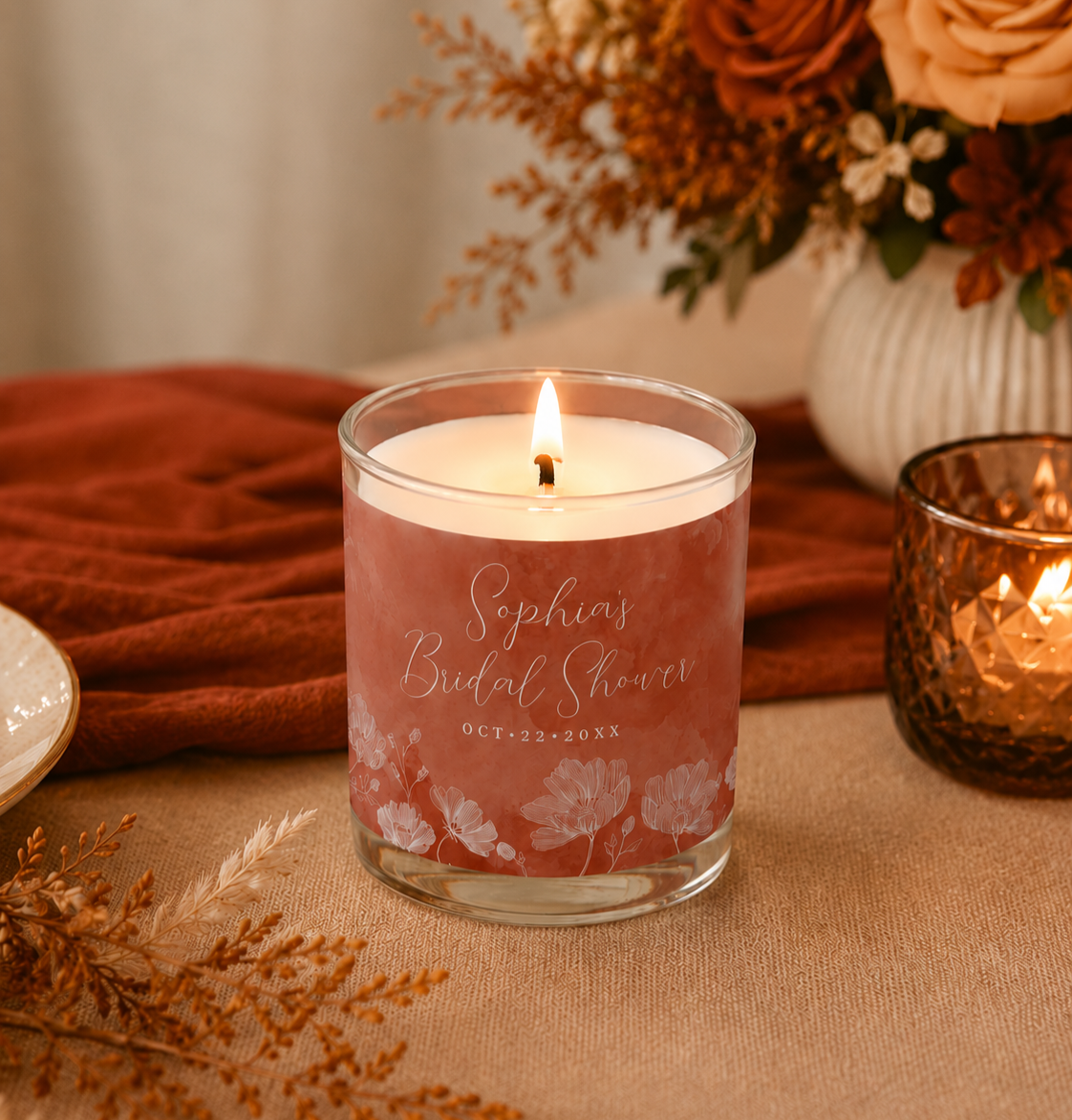 Close-up of a personalized terracotta bridal shower candle favor styled on a warm autumn-inspired tablescape with soft candlelight, florals, and cozy romantic décor.