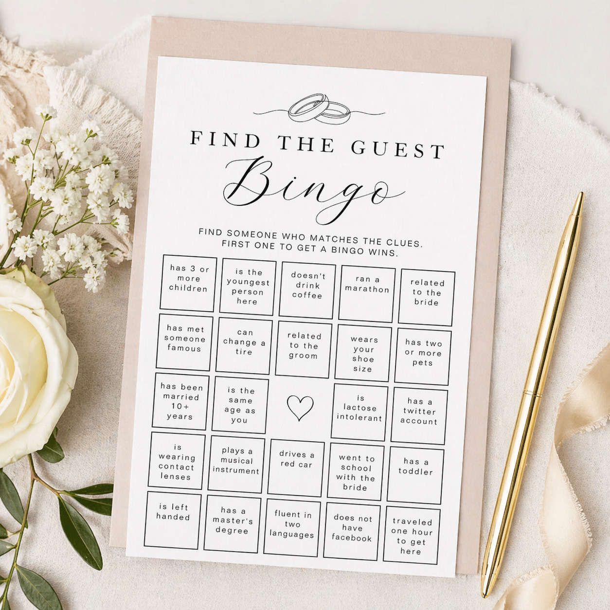 Elegant Find the Guest Bingo bridal shower game card with blush backing sheet, gold pen, white roses, and neutral fabric styling. Printable bridal shower mingle game with bingo grid and guest clue prompts in a modern black and white design.